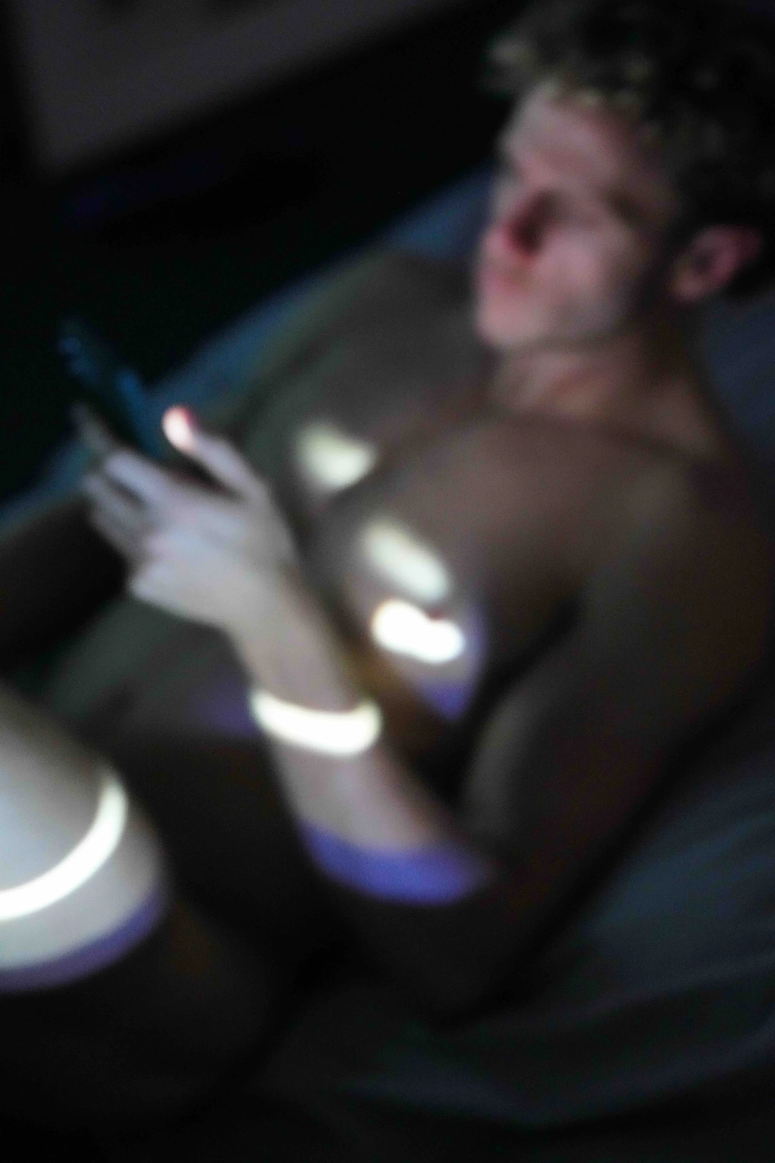 A person holding a smartphone in their hand, with the screen illuminated, in a dark setting.