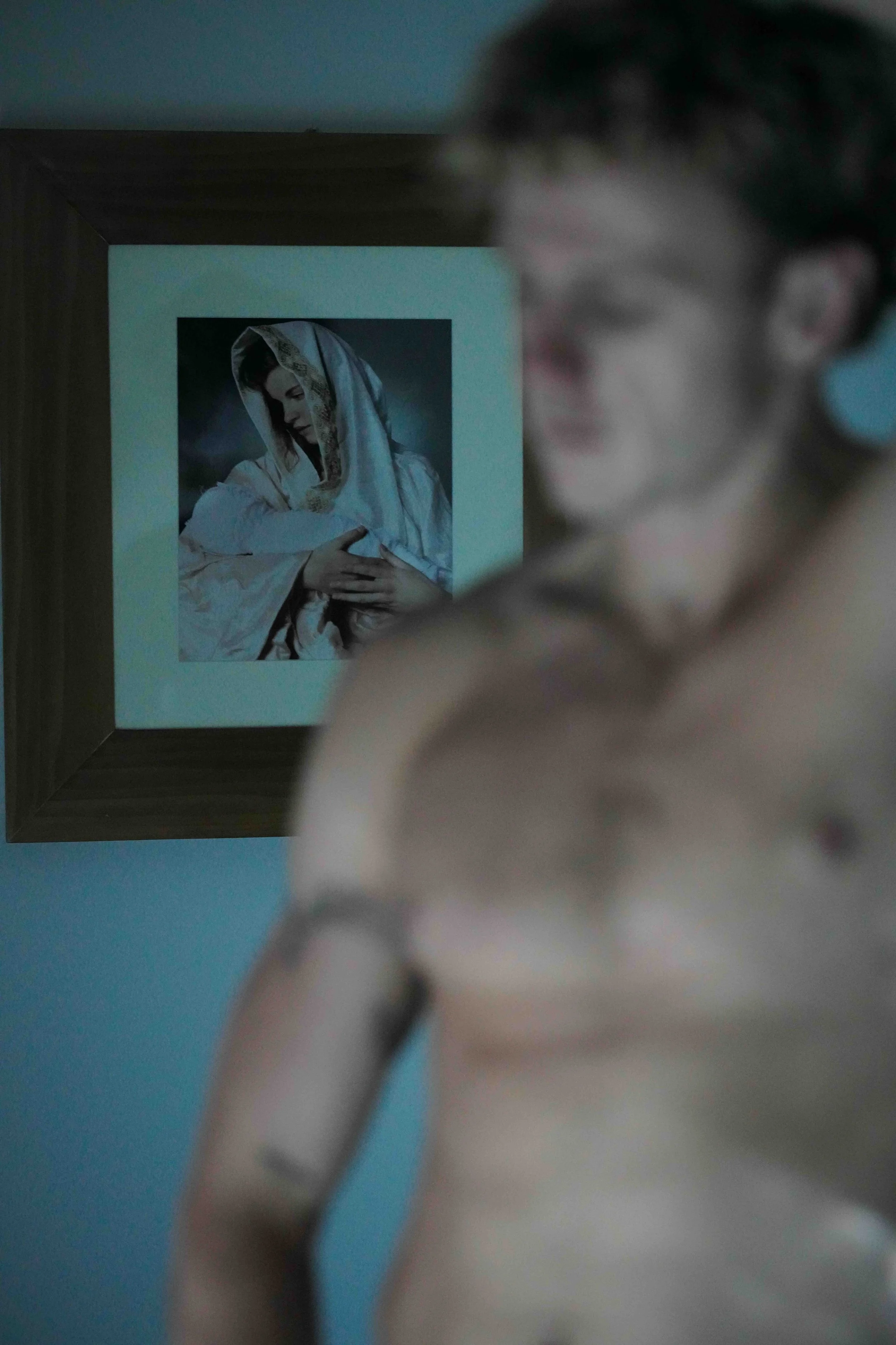 A person holding a chain in front of a framed picture of a woman with a headscarf. The picture is mounted on a wall.