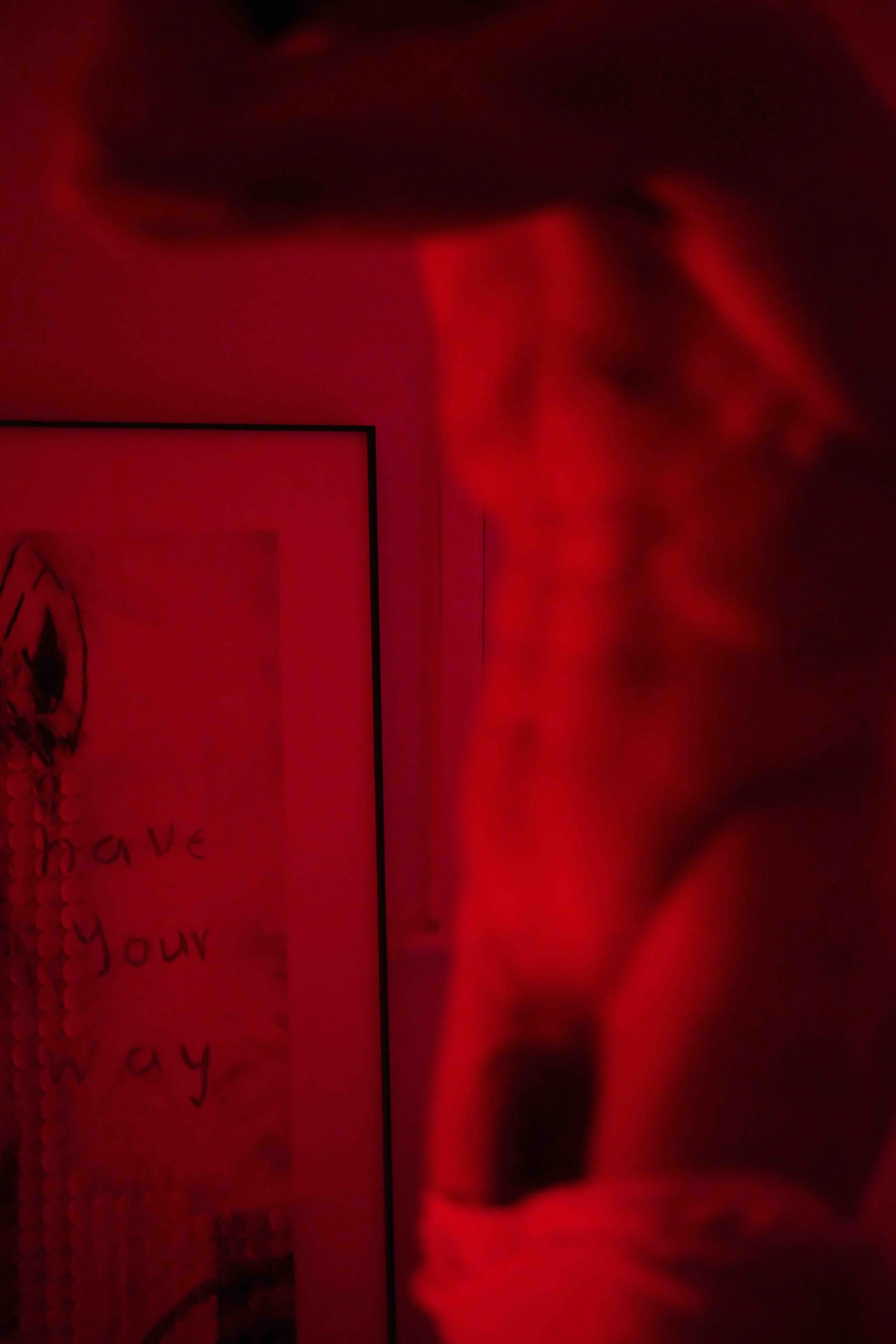 A red-lit room with a framed illustration of a heart with a banner and handwritten message on the wall.