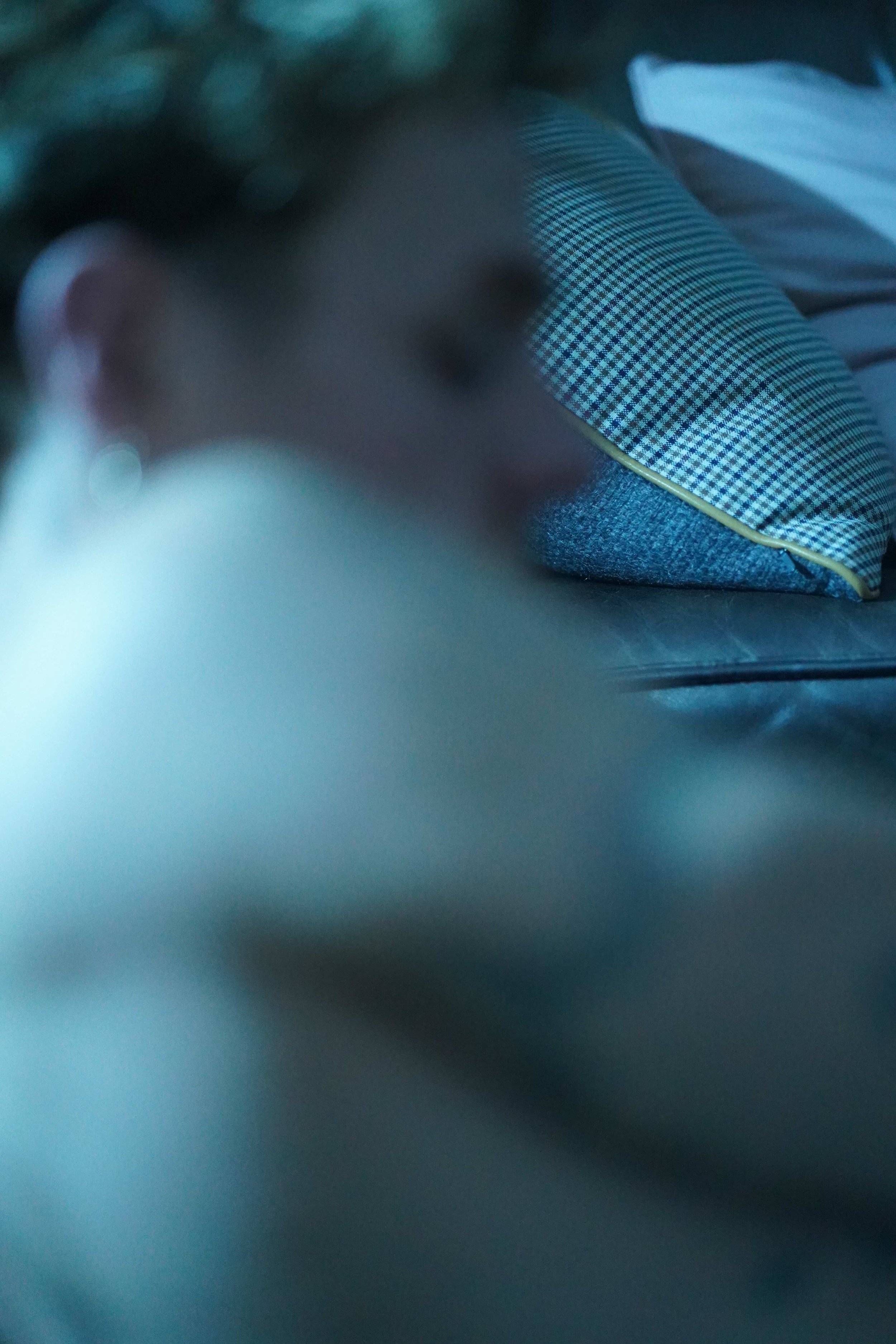 Close-up of a person wearing checkered and gray clothing, laying down with their eyes closed, with blurred foreground and background.