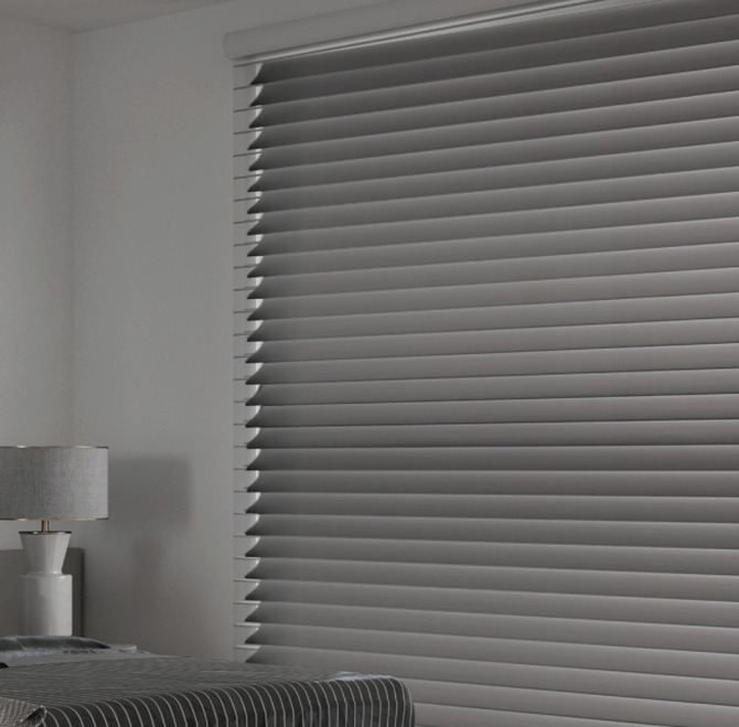 Close-up of silver window blinds covering a window in a modern bedroom with white walls and a desk lamp.
