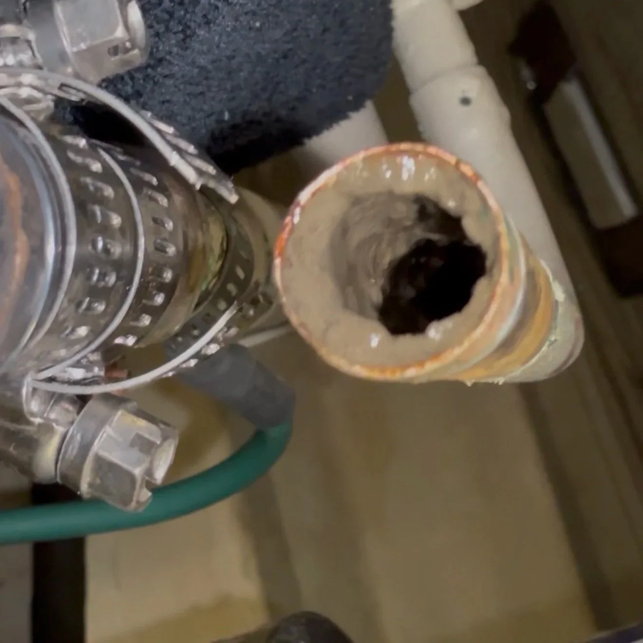 Close-up of a rusted, corroded pipe connected to a metal fitting, with a black object visible inside the pipe.