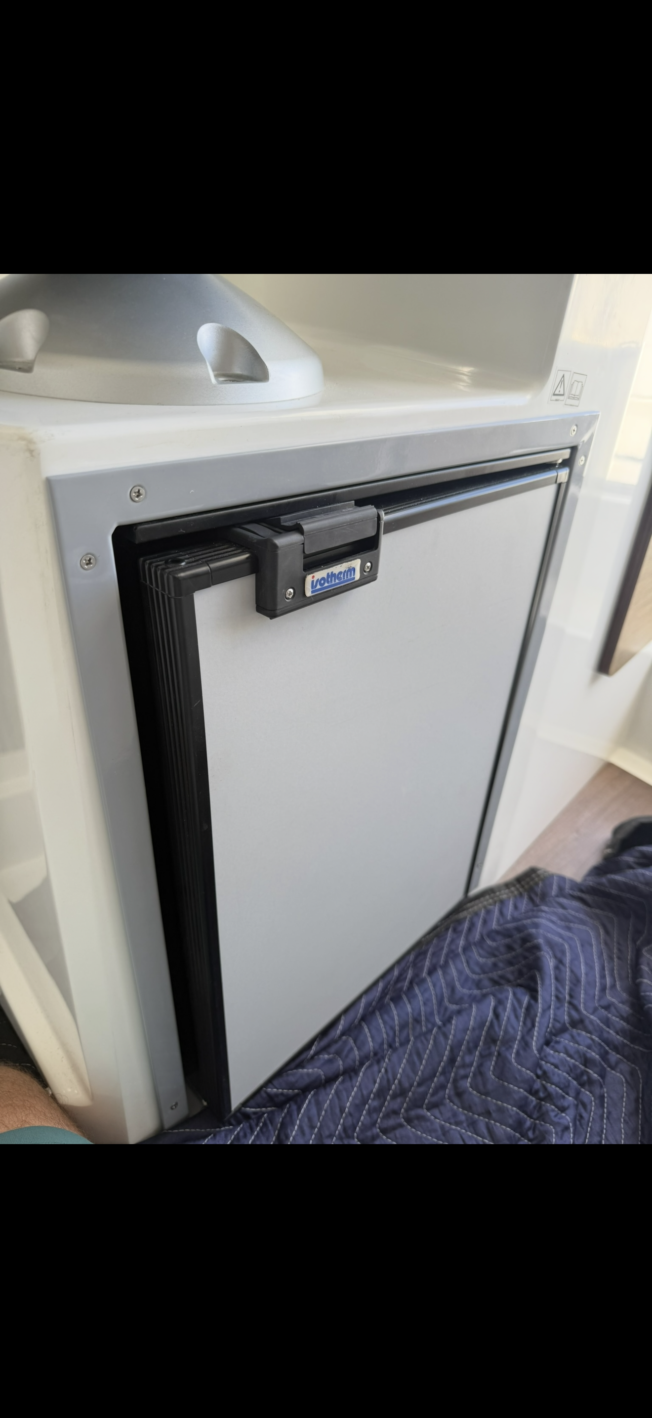 A small refrigerator with a black lock on its door, situated next to a metal surface, possibly a sink or counter.