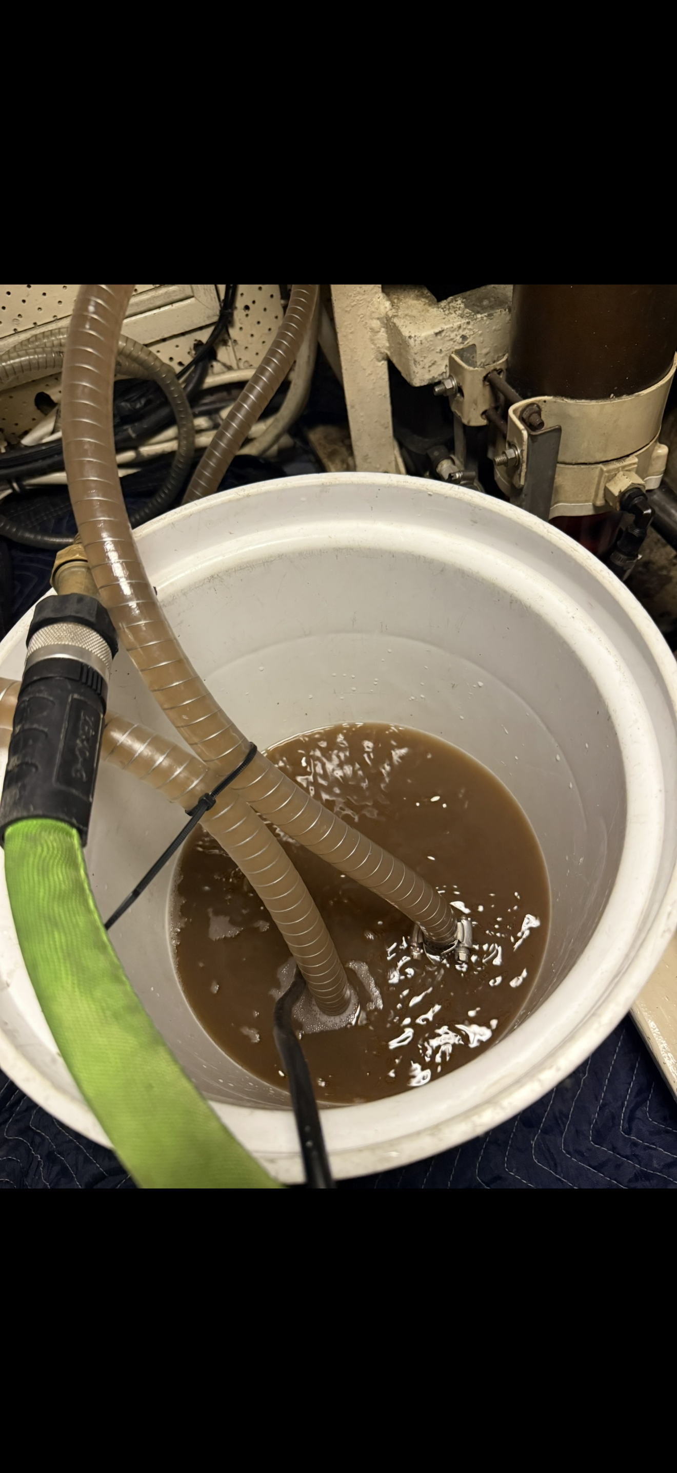 A white bucket filled with brownish wastewater and hoses connected to a machine.