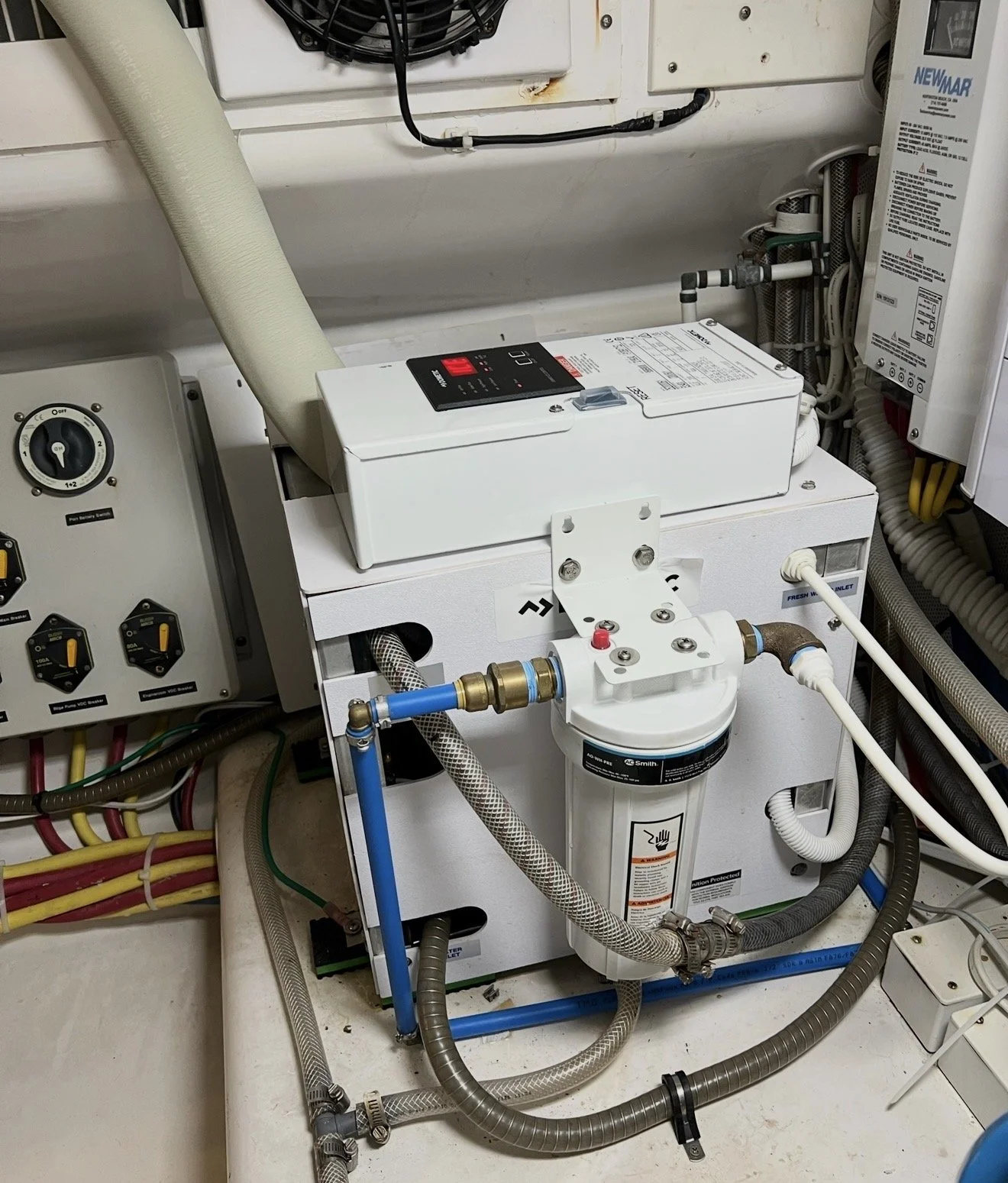 A mechanical water treatment system with various pipes, gauges, a filter, and control panels installed on a white surface in a maintenance room.