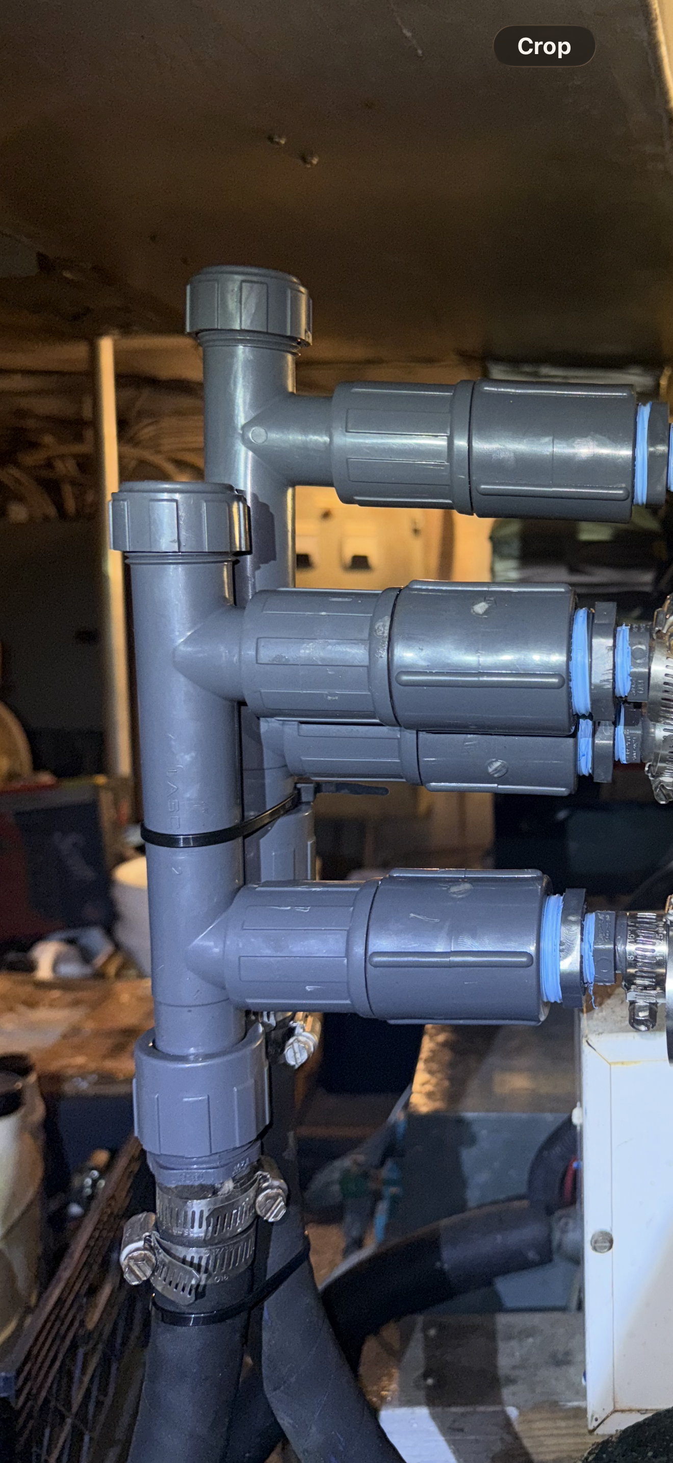 Close-up of gray PVC barbed fittings and hoses connected in a plumbing or irrigation system, with a background of storage shelves and miscellaneous items.