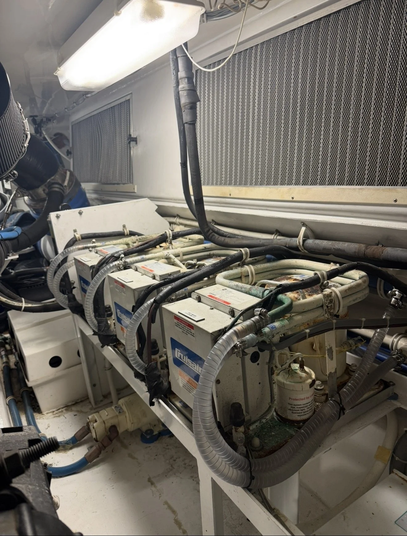 The image shows a close-up view of industrial HVAC equipment with multiple refrigerant pipes, control units, and filters in a mechanical room or server room. There are black hoses, metal pipes, and electrical wiring connected to the units.