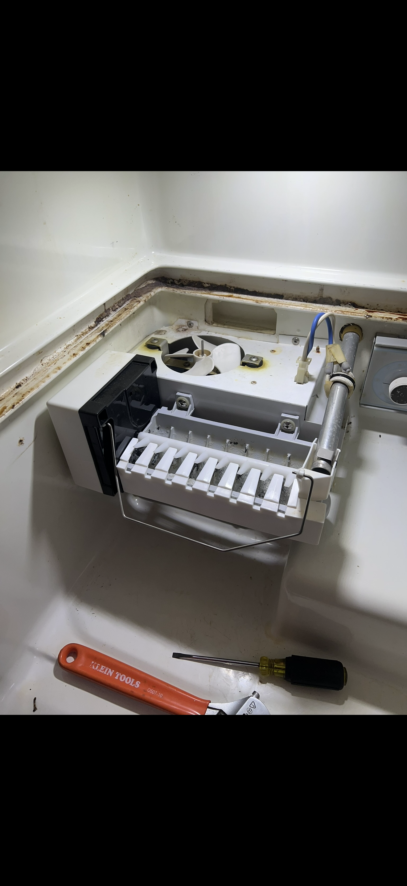 Disassembled dishwasher with internal components exposed, tools including a screwdriver and a wrench nearby.