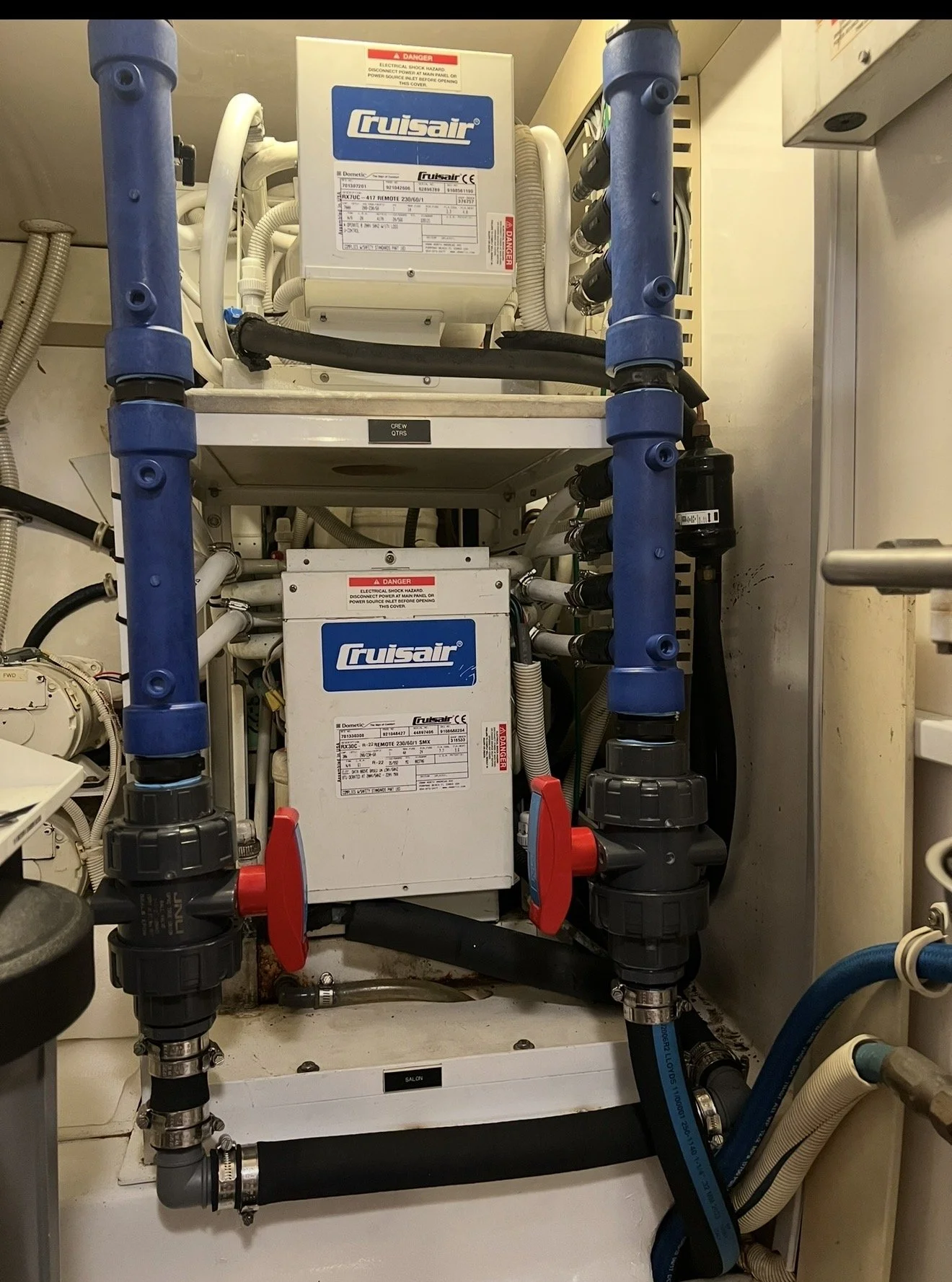 A mechanical system with two white box-shaped units labeled 'Cruisair', connected by multiple black, white, and blue pipes, valves, and fittings, mounted within a confined space.
