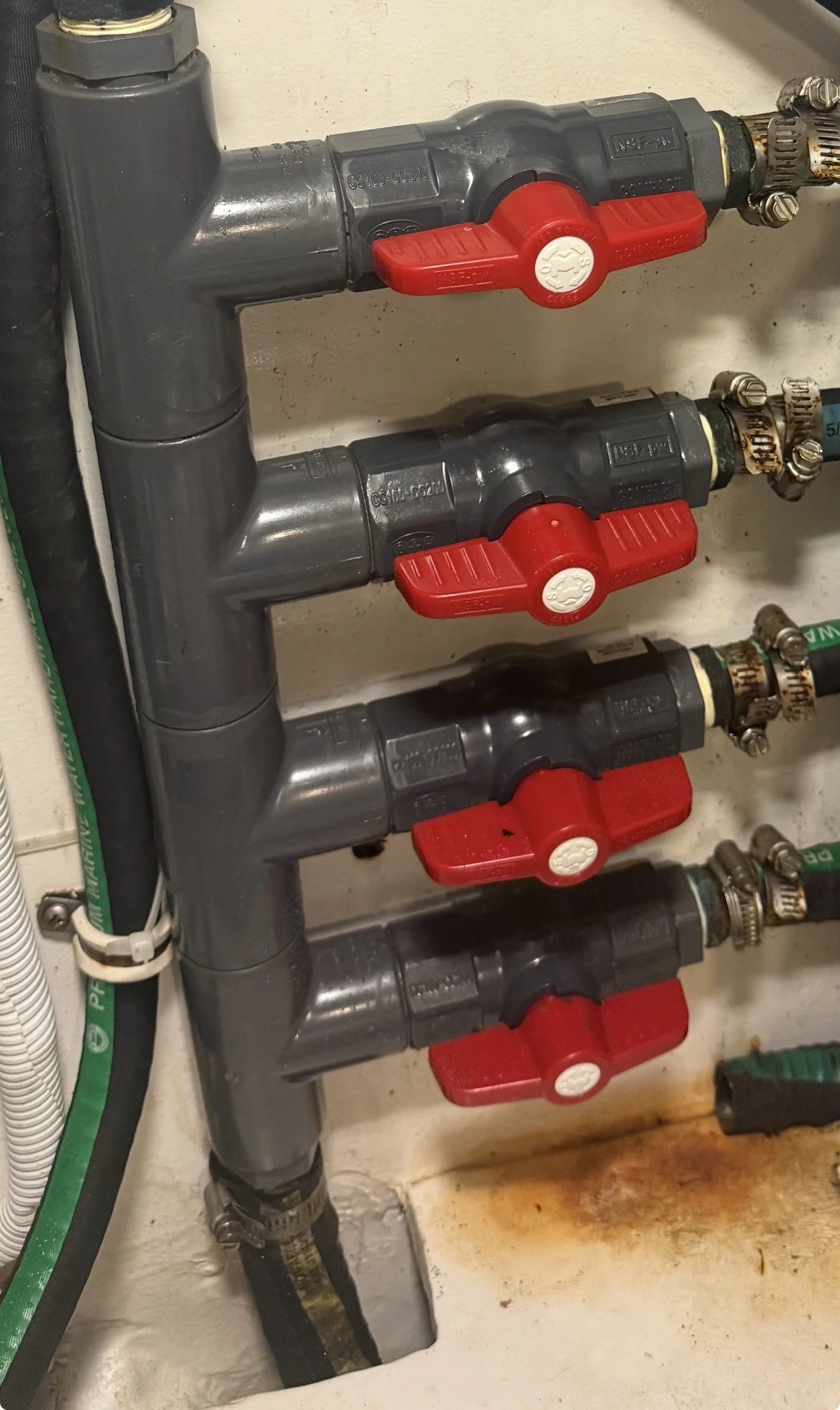 Multiple gray water valves with red handles in a plumbing system, connected to pipes on a wall.