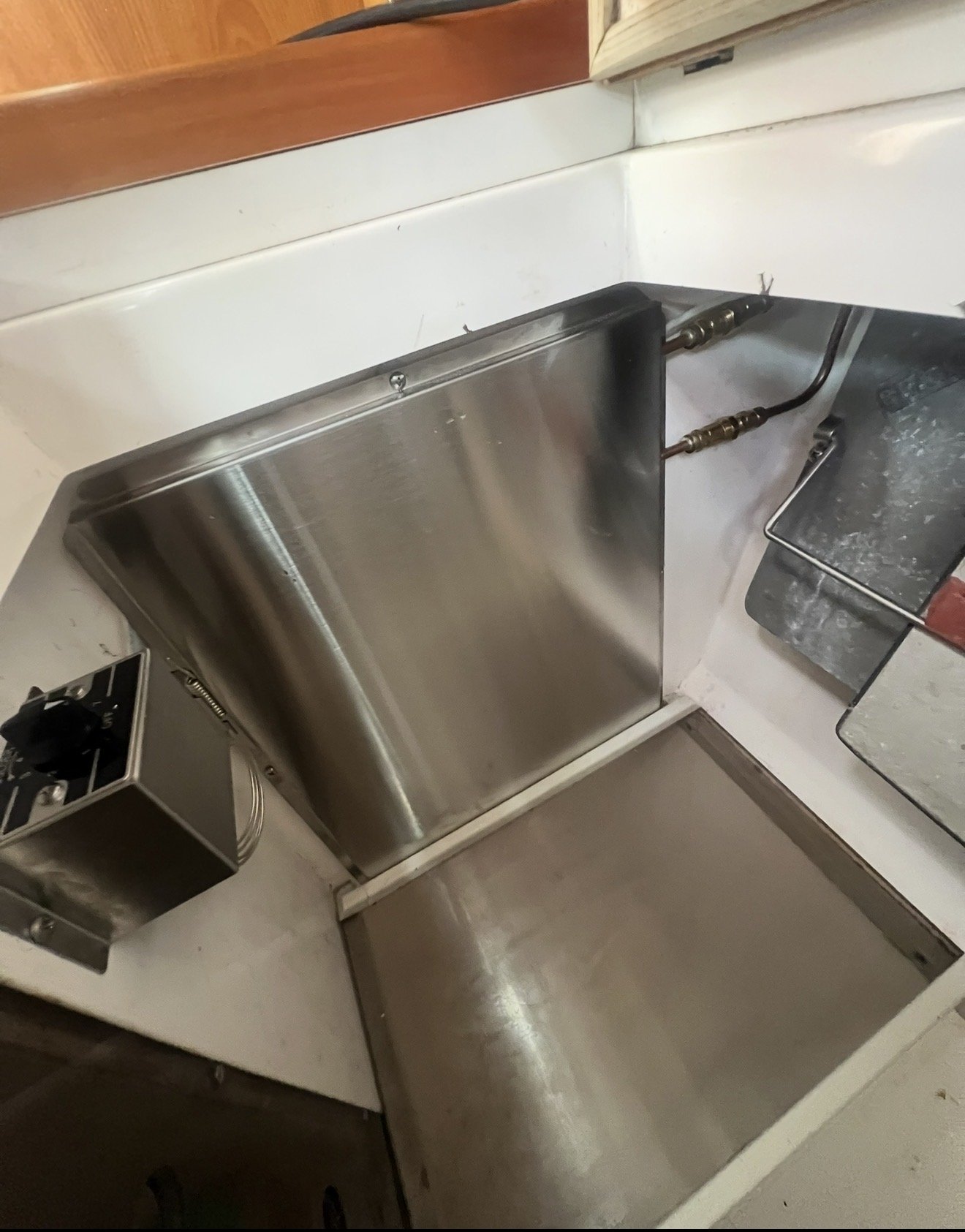 A stainless steel commercial dishwasher next to a white countertop and a black grill or oven with a metal rack. The area shows signs of ongoing cleaning or maintenance, with splashes of water or soap on the surfaces.
