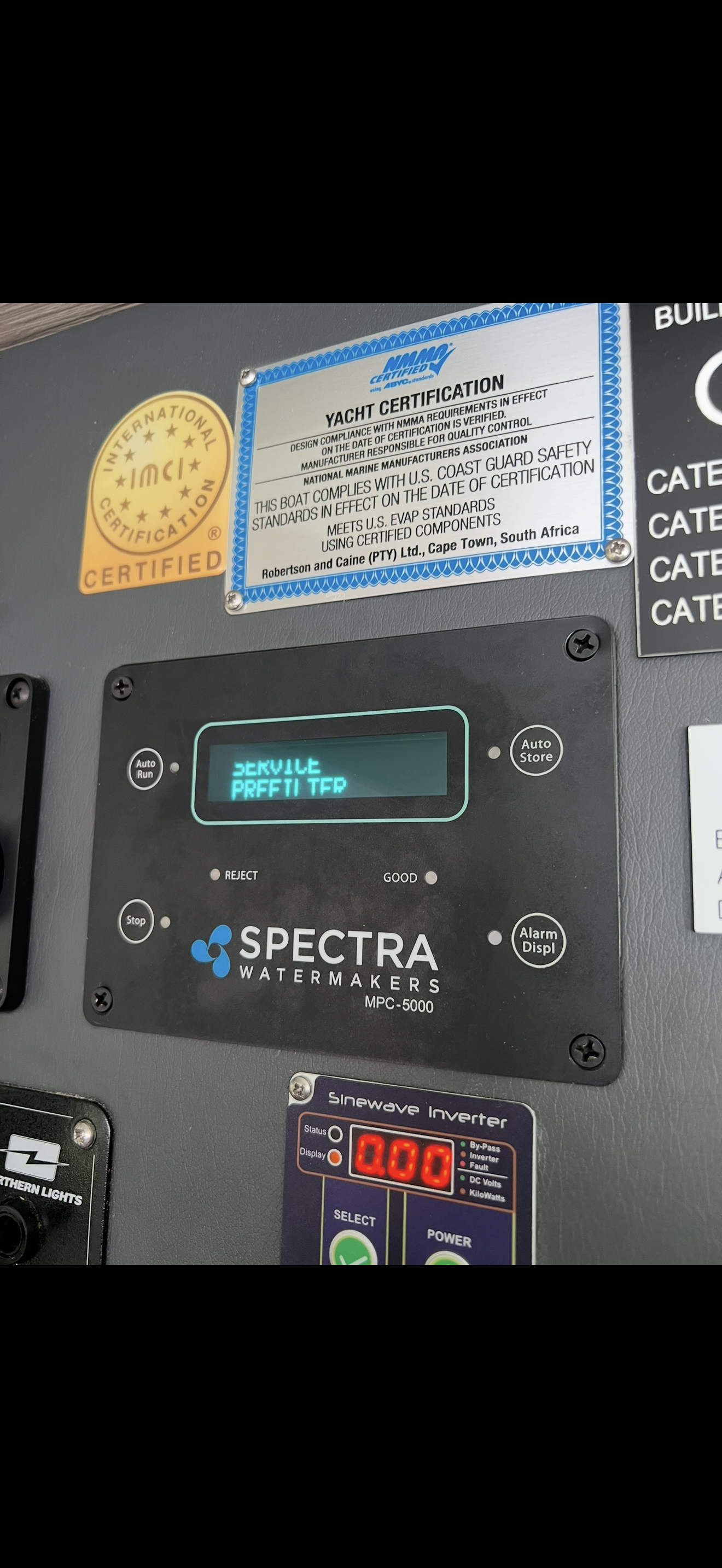 Close-up of a watermaker control panel displaying 'SERVICE PERFORM' on the screen, with certification labels above.