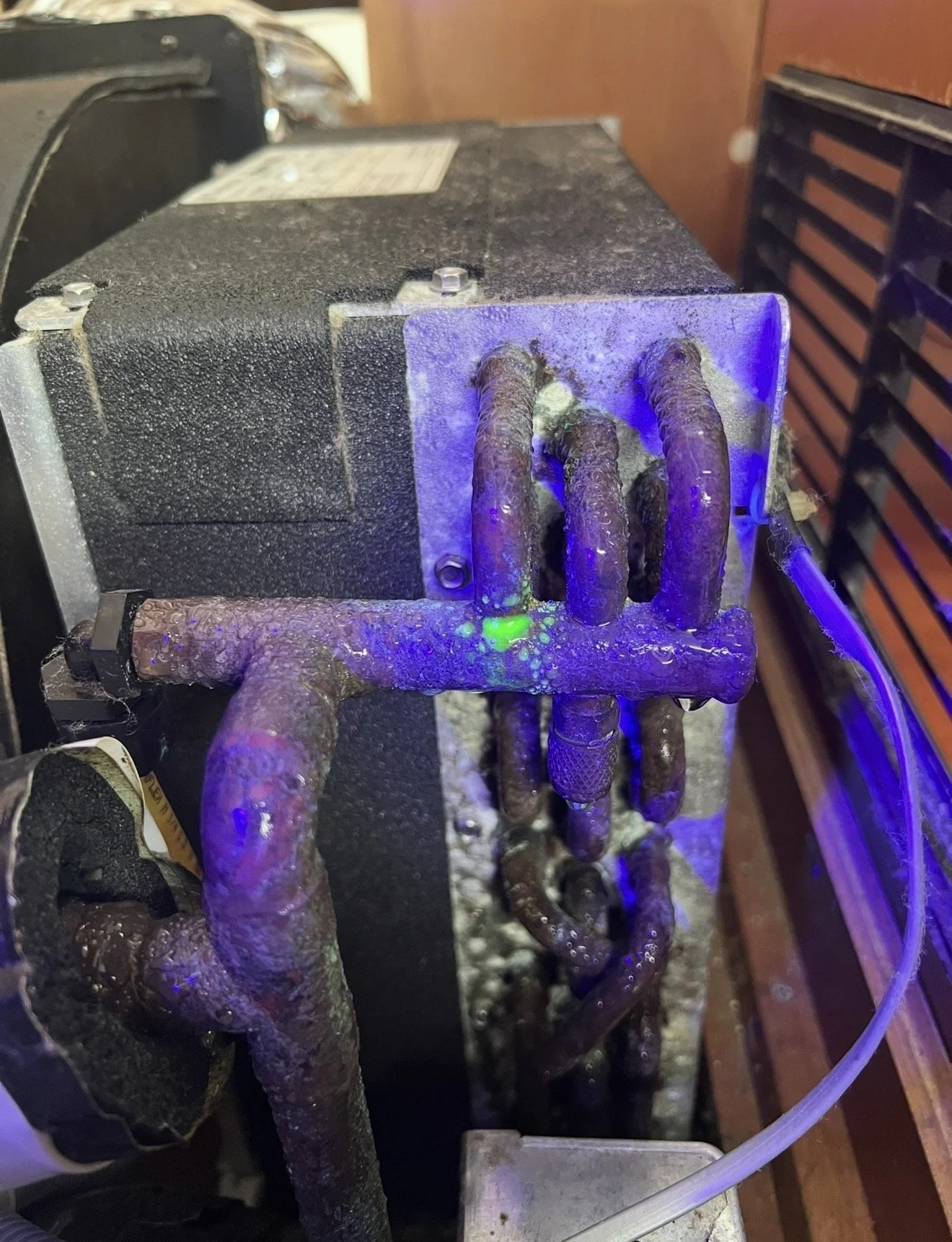 Close-up of a large, rusted industrial machine with multiple corroded pipes and tubes, some glowing purple and green under ultraviolet light.