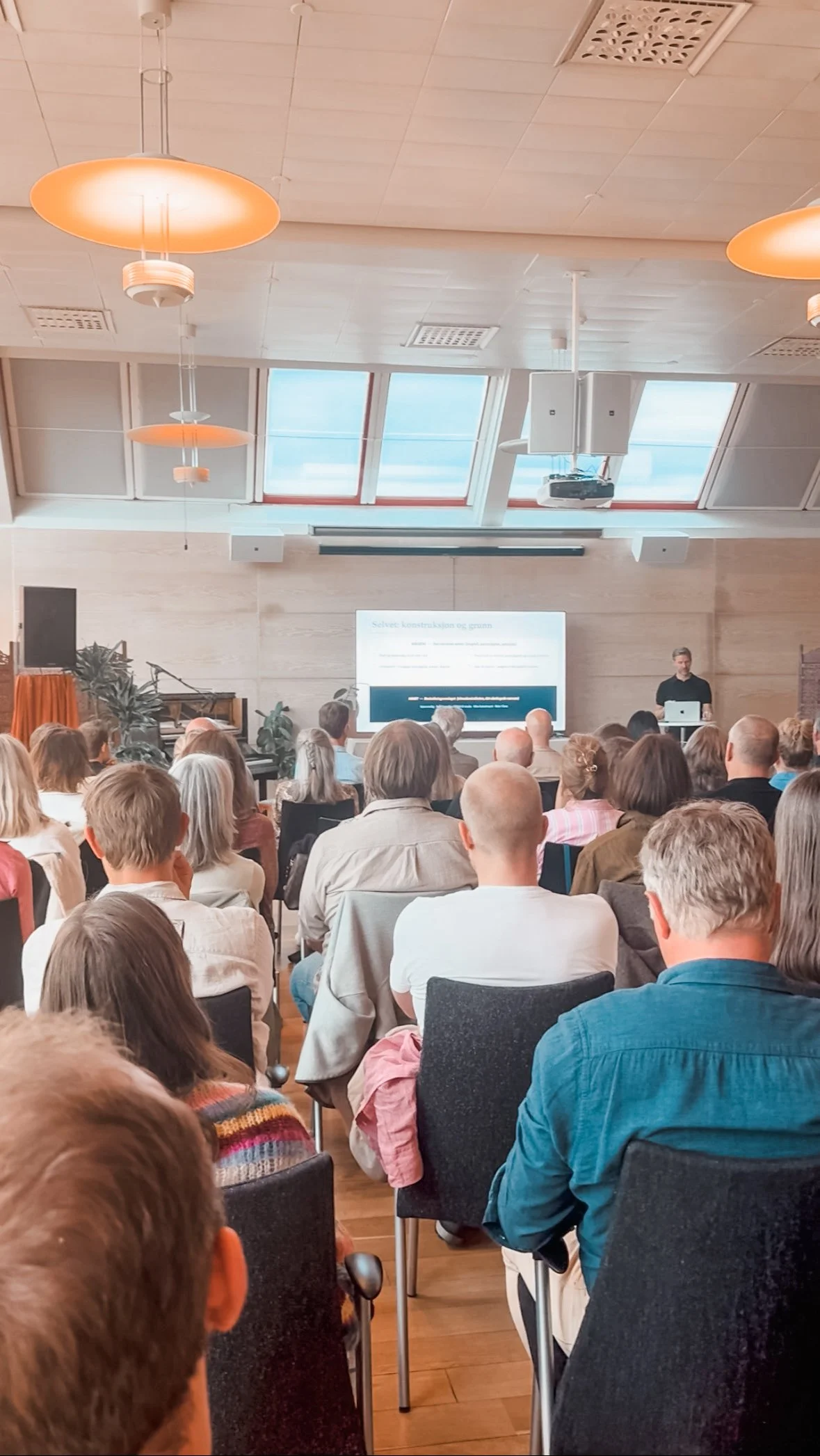 A large audience seated in The Glass Garden at CONOS in central Oslo for an event with an international guest speaker.