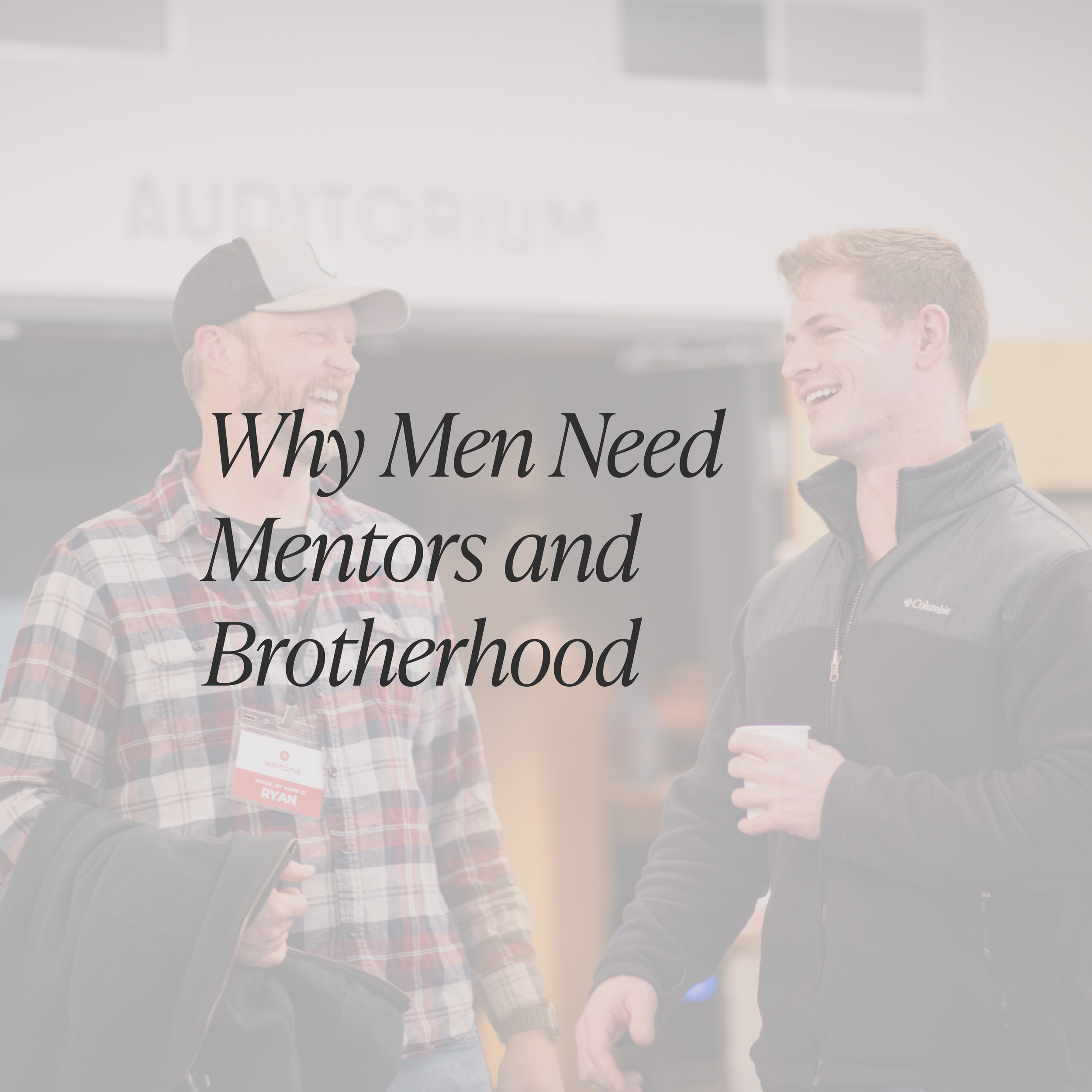 Two men smiling and chatting indoors, one wearing a baseball cap and plaid shirt, the other wearing a black jacket, with partially visible text on the wall behind them reading "Why Men Need Mentors and Brothers".