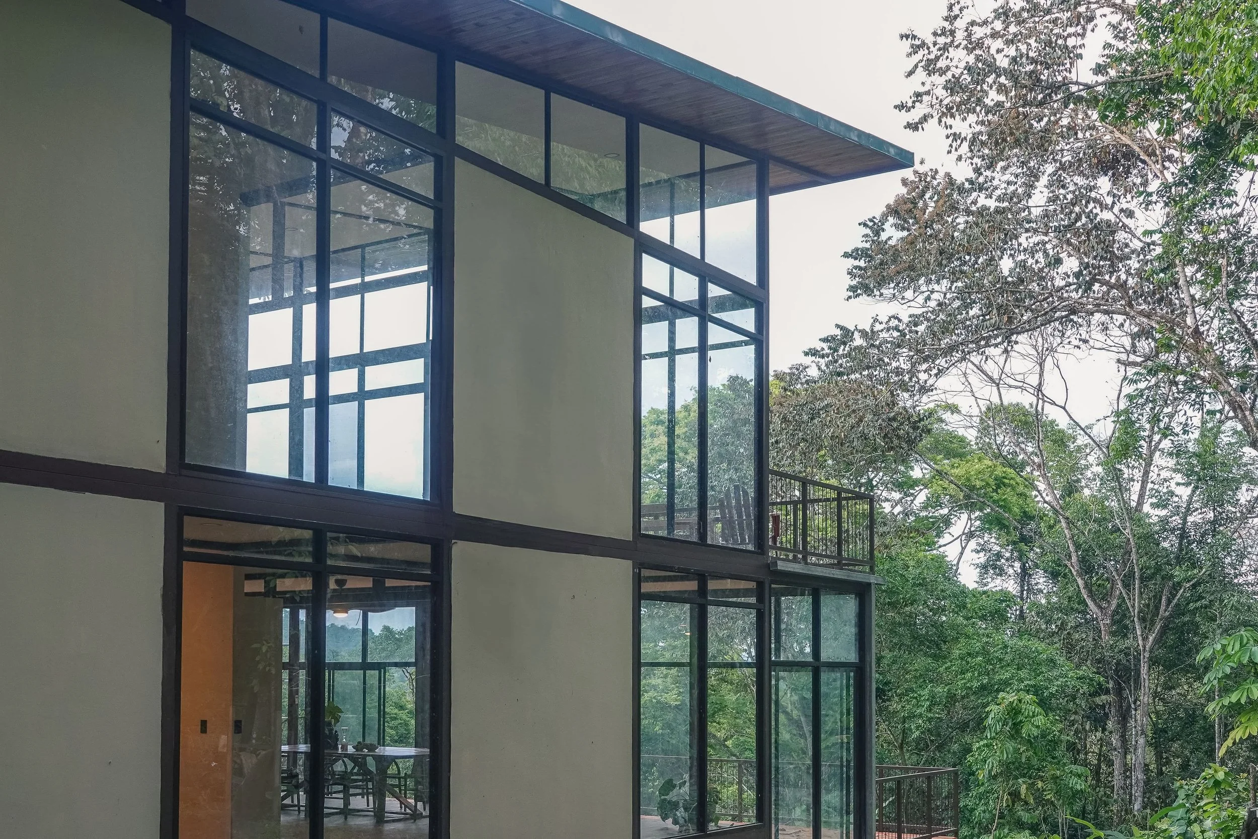 Modern house with large glass windows surrounded by trees in a lush green setting.