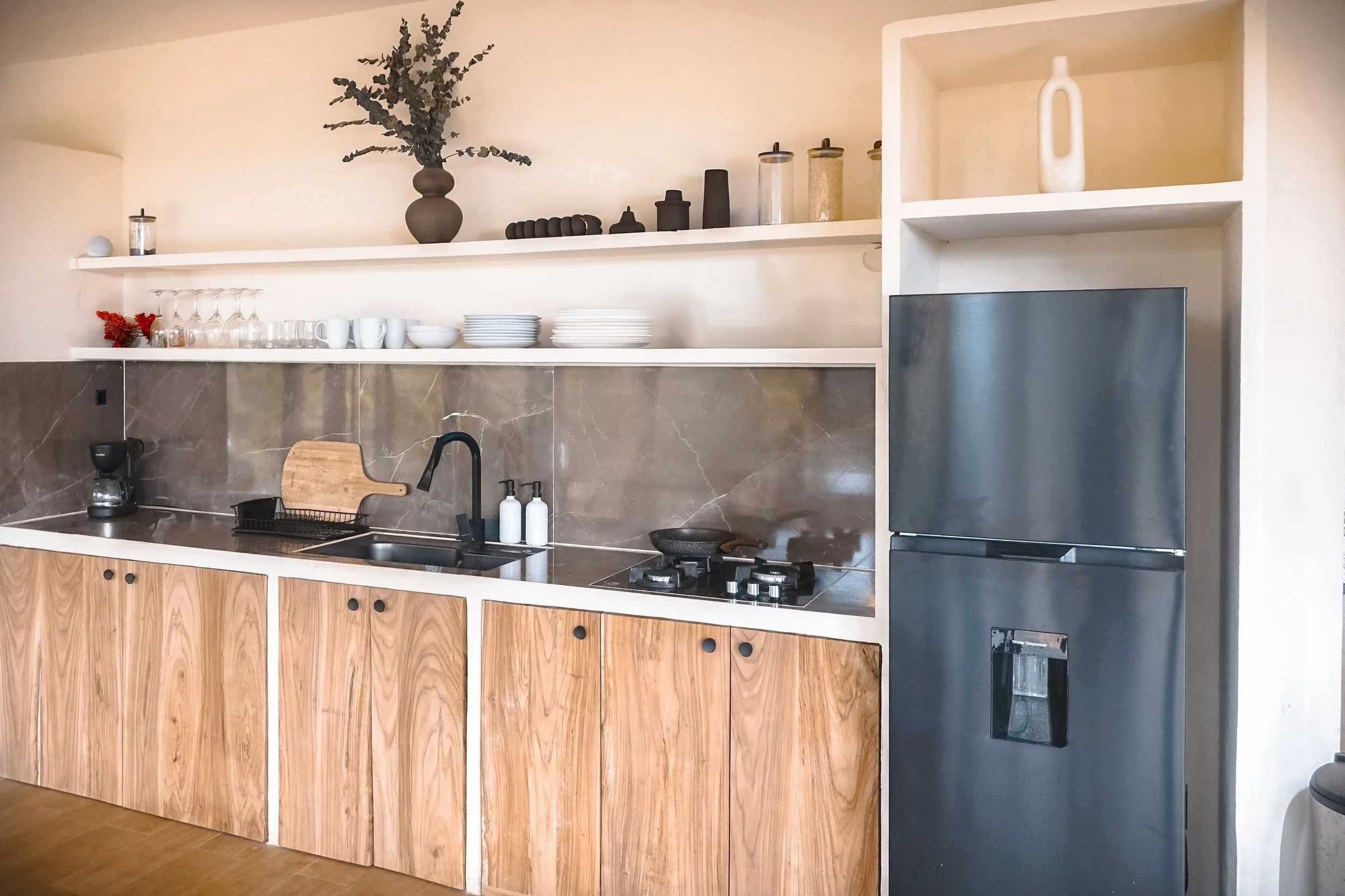 Modern kitchen with wooden cabinets, a black sink, a coffee maker, glassware, plates, and a black refrigerator.