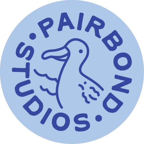 Circular logo with blue background featuring an albatross head in the center and the text "PAIRBOND STUDIOS" around the albatross in dark blue letters.
