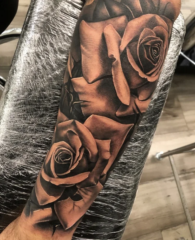 A detailed black and gray tattoo of two roses on a person's arm.