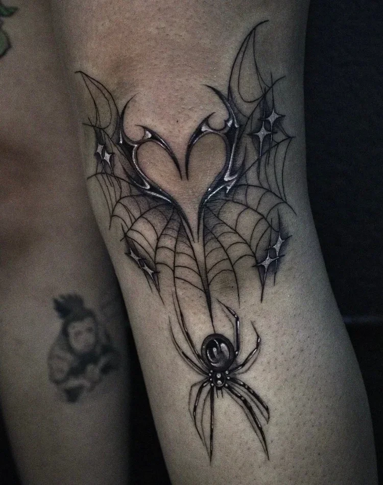 A tattoo of a spider hanging from a web, with the web forming a heart shape.