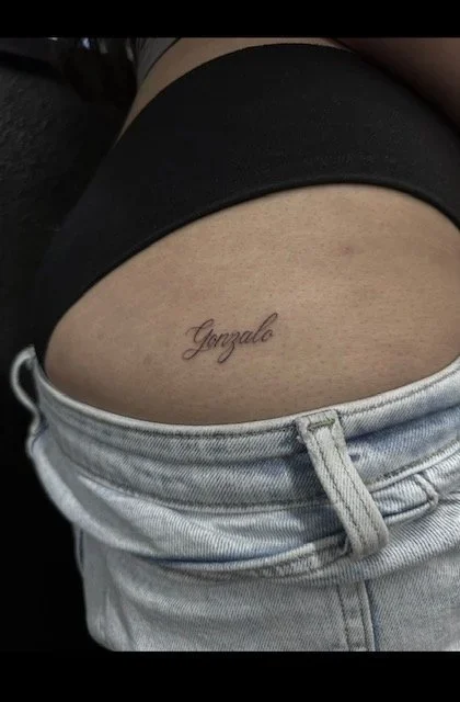 A person's lower back and waist showing a tattoo that says 'Gonzalo' in cursive script.