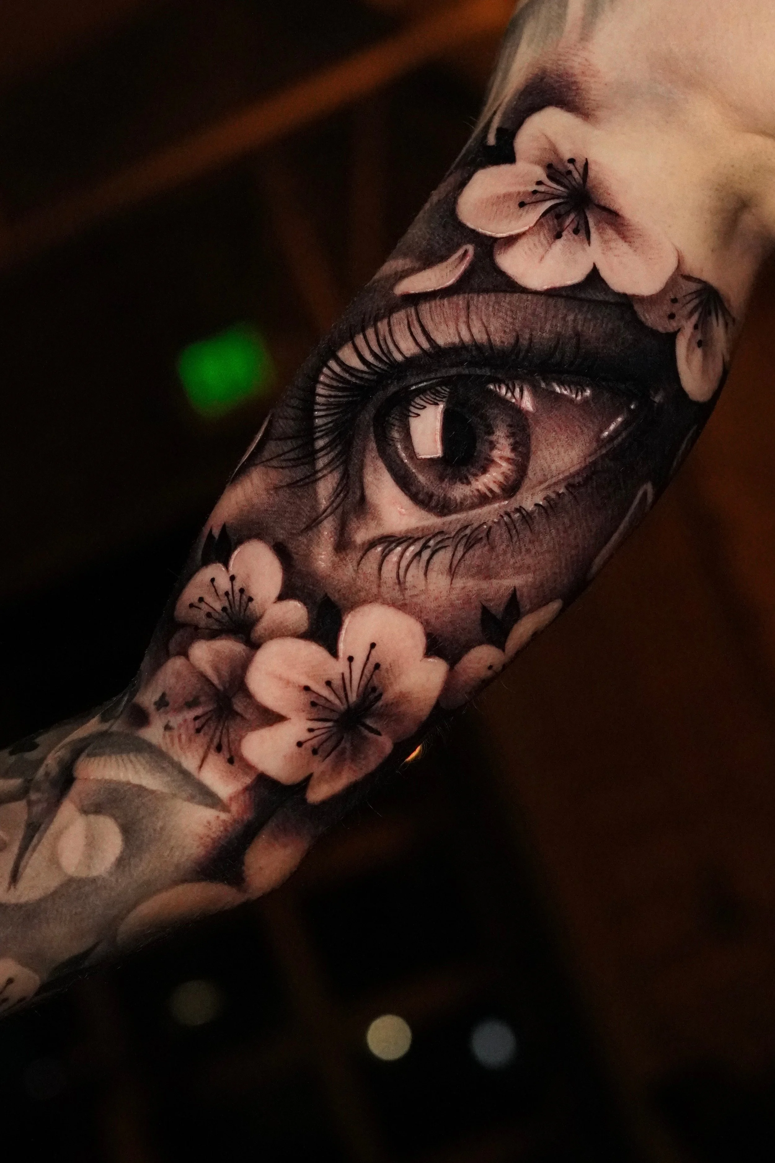 Close-up of a person's arm tattoo featuring a large eye surrounded by pink flowers with black details and shading.
