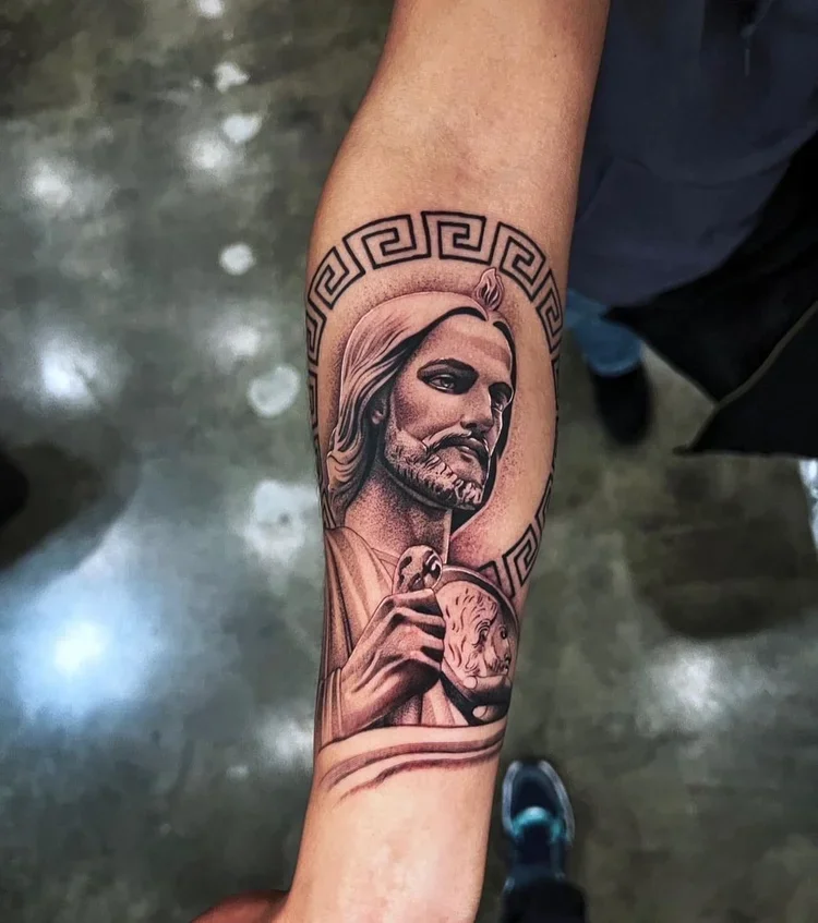 Tattoo of a man with long hair and a beard, holding a skull with a lion face, surrounded by a Greek key pattern.