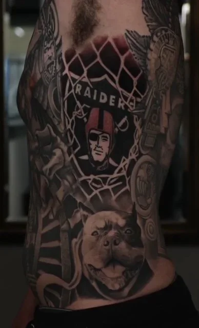 Tattoo on a person's side featuring a Raiders logo, a woman's face with a pink headband, and a dog's face at the bottom.