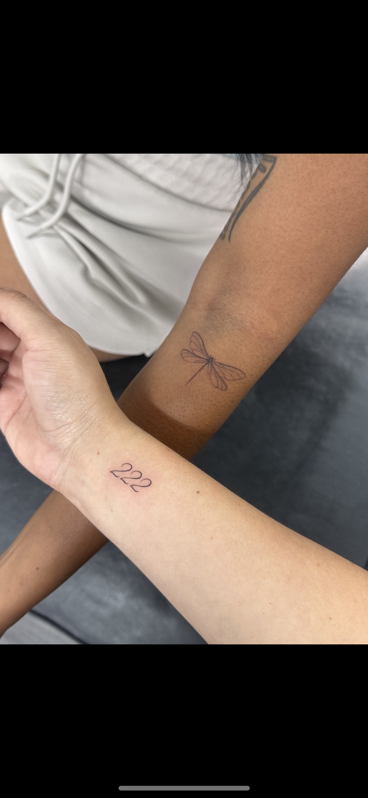 Close-up of two arms with tattoos, one with a dragonfly tattoo and the other with the number 222 tattoo.