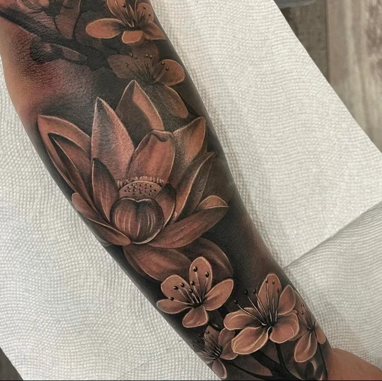 Close-up of a black tattoo sleeve featuring detailed brown and tan lotus flowers and butterflies.