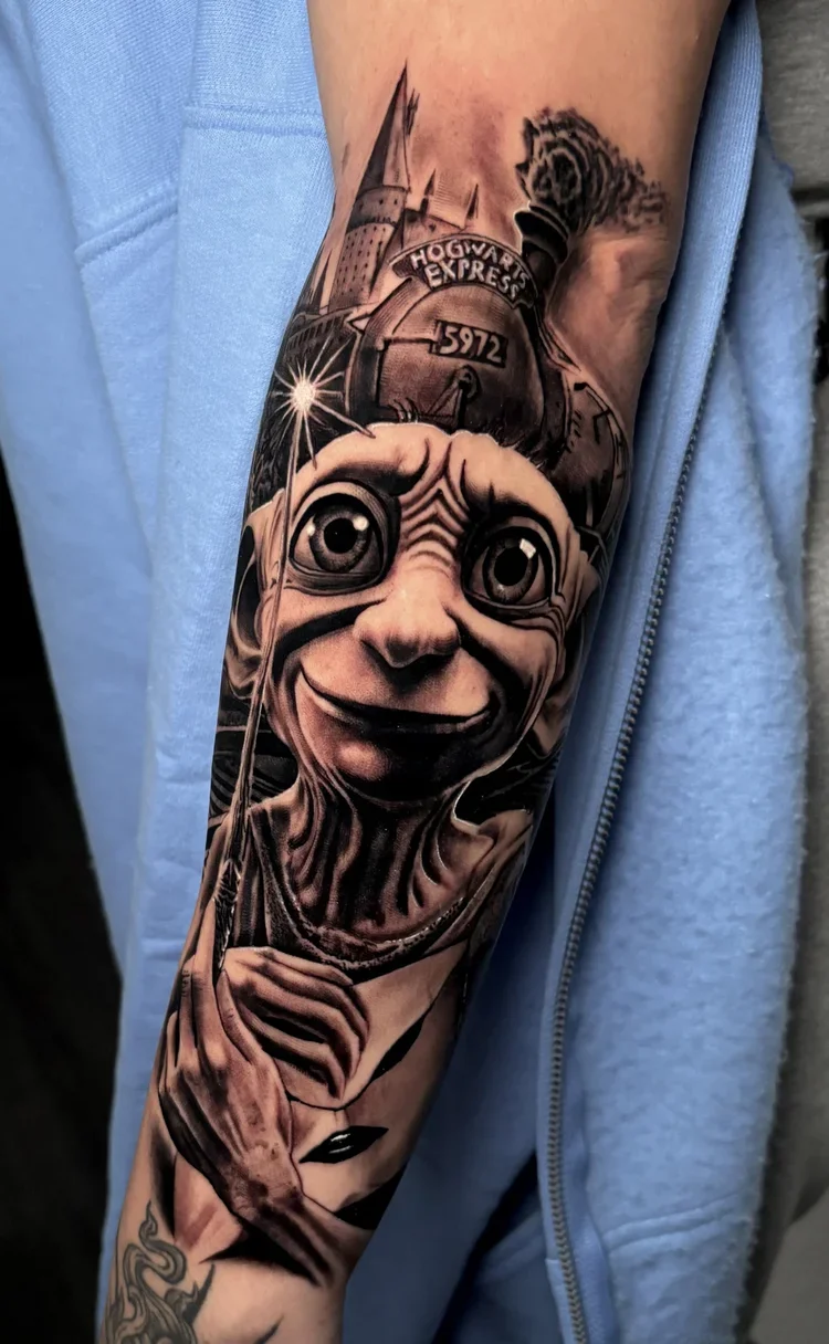 Black and gray tattoo of a whimsical character with large eyes and a wide smile, holding a wand, with a Hogwarts Express train and castle in the background.