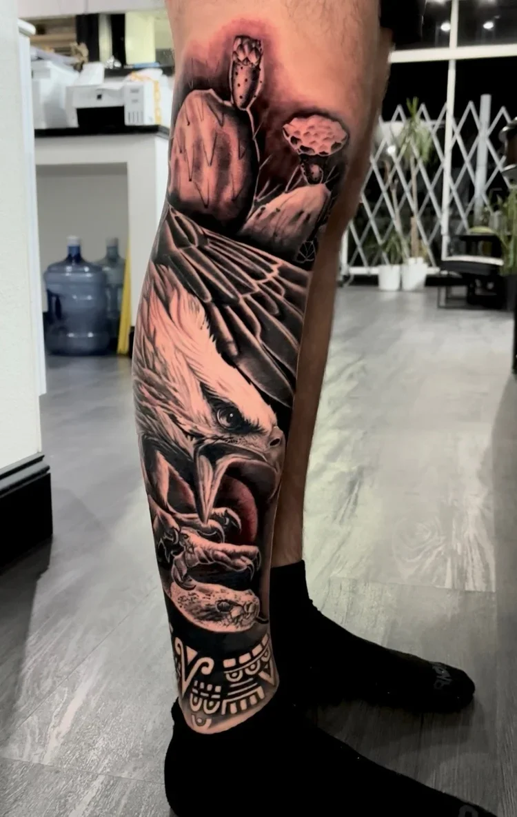 Black and gray tattoo sleeve featuring an eagle, a fierce lion, and tribal patterns on a person's leg.