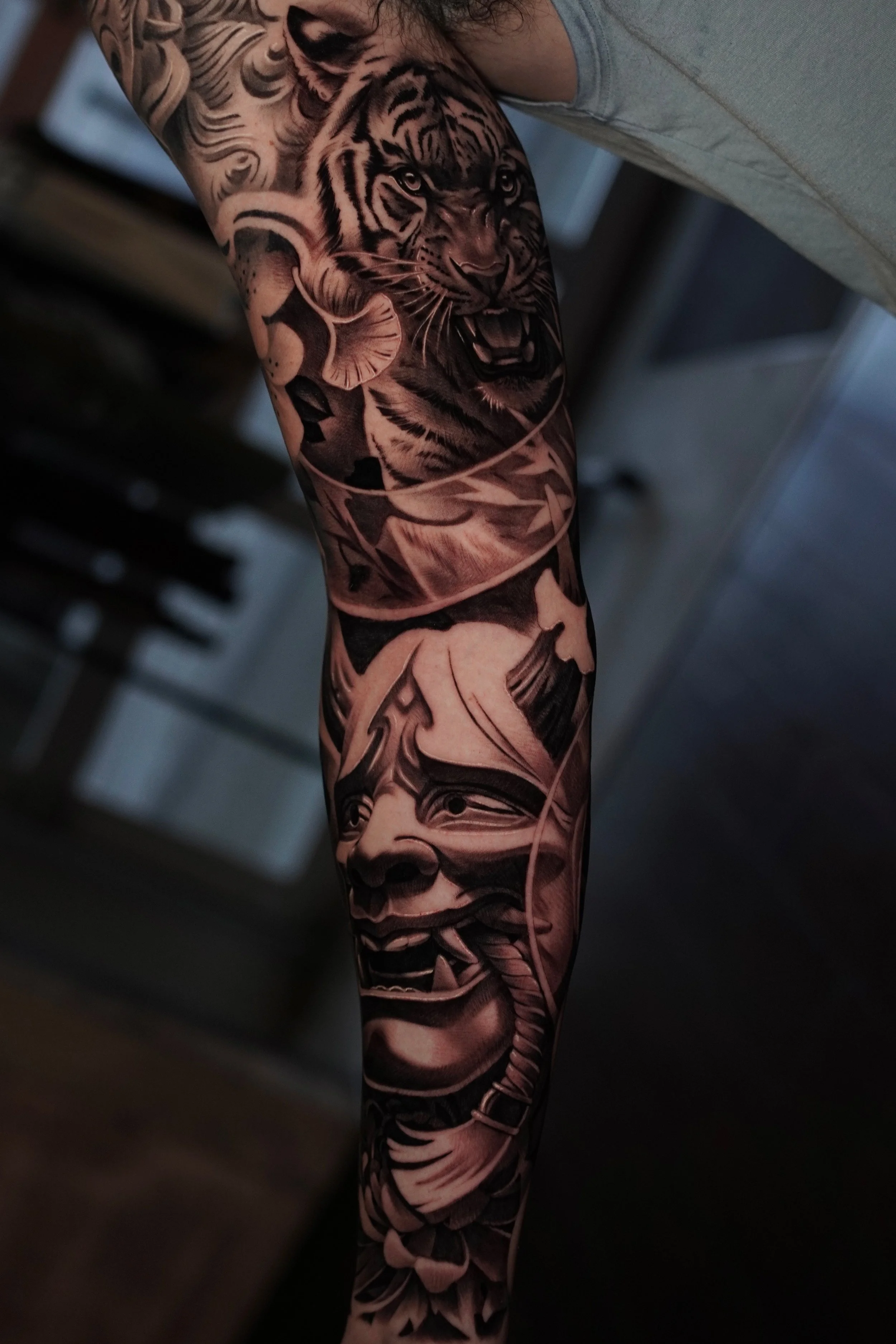 A detailed black and gray tattoo of a tiger's face, with its mouth open, on a person's arm.