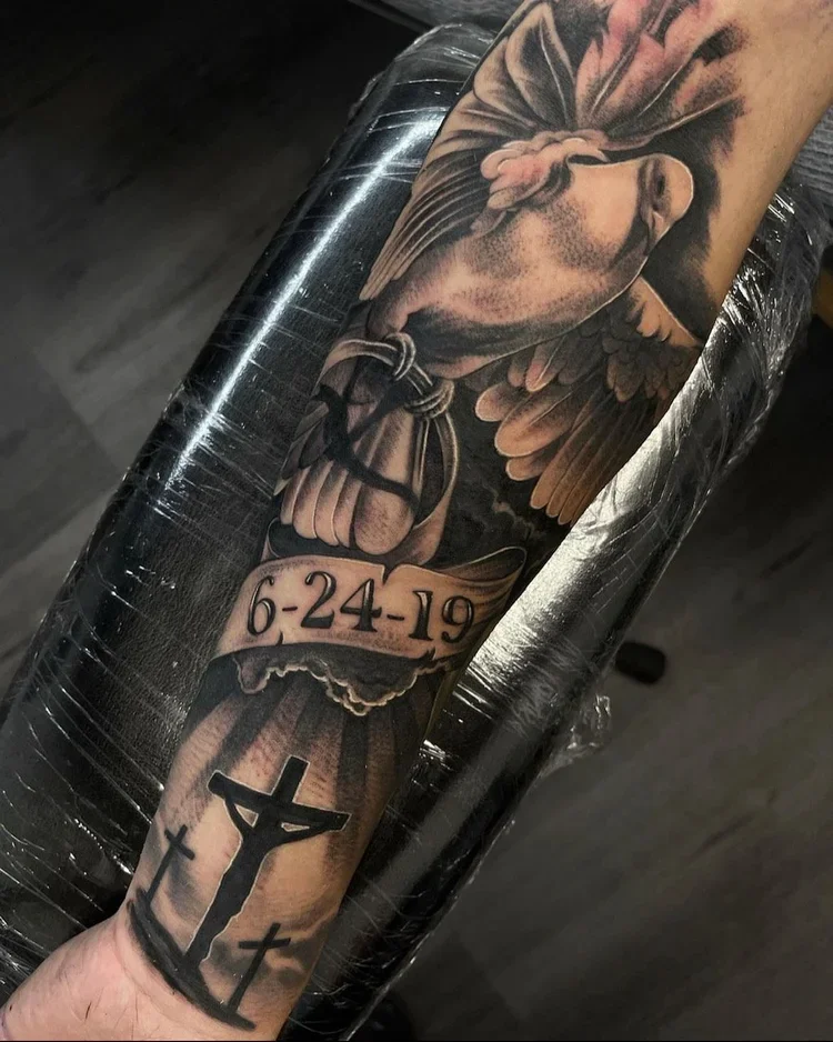 Black and gray tattoo sleeve featuring a winged horse, a ribbon with the date 6-24-19, and a Christian cross with a figure on it.