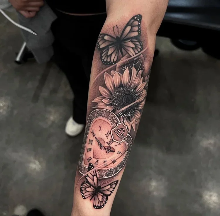 Tattoo featuring a sunflower, a pocket watch, and two butterflies on a forearm.