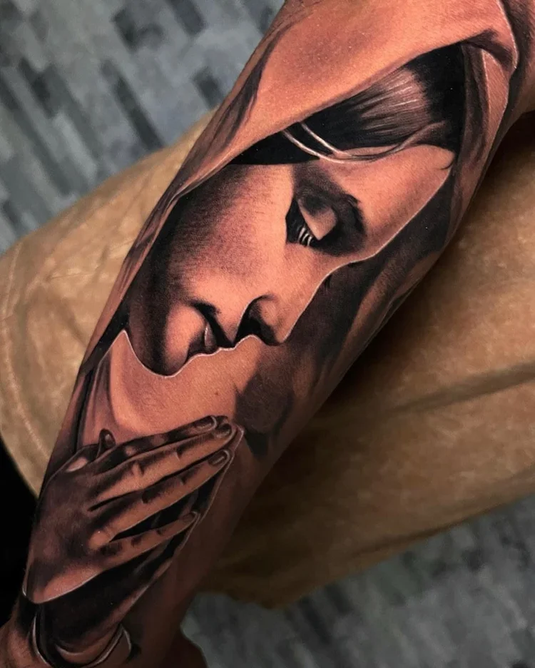 Close-up of a realistic black and gray tattoo depicting a woman in profile with her eyes closed, holding her hands together near her lips.