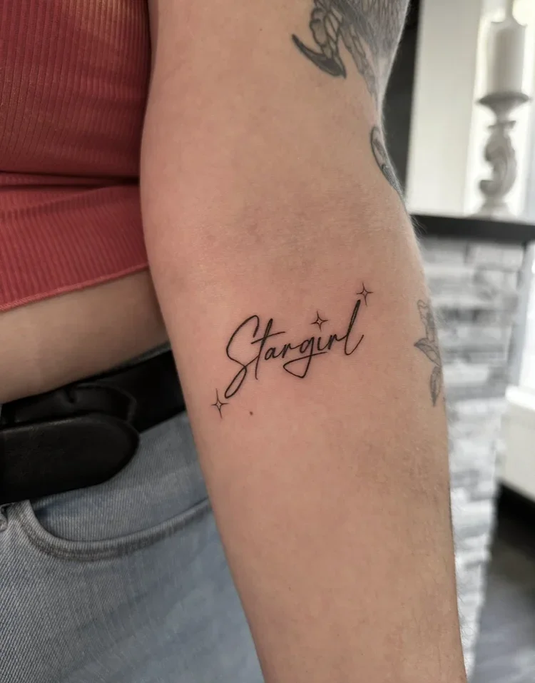 Tattoo on person's upper arm that reads 'Stargirl' with small star graphics around the text.