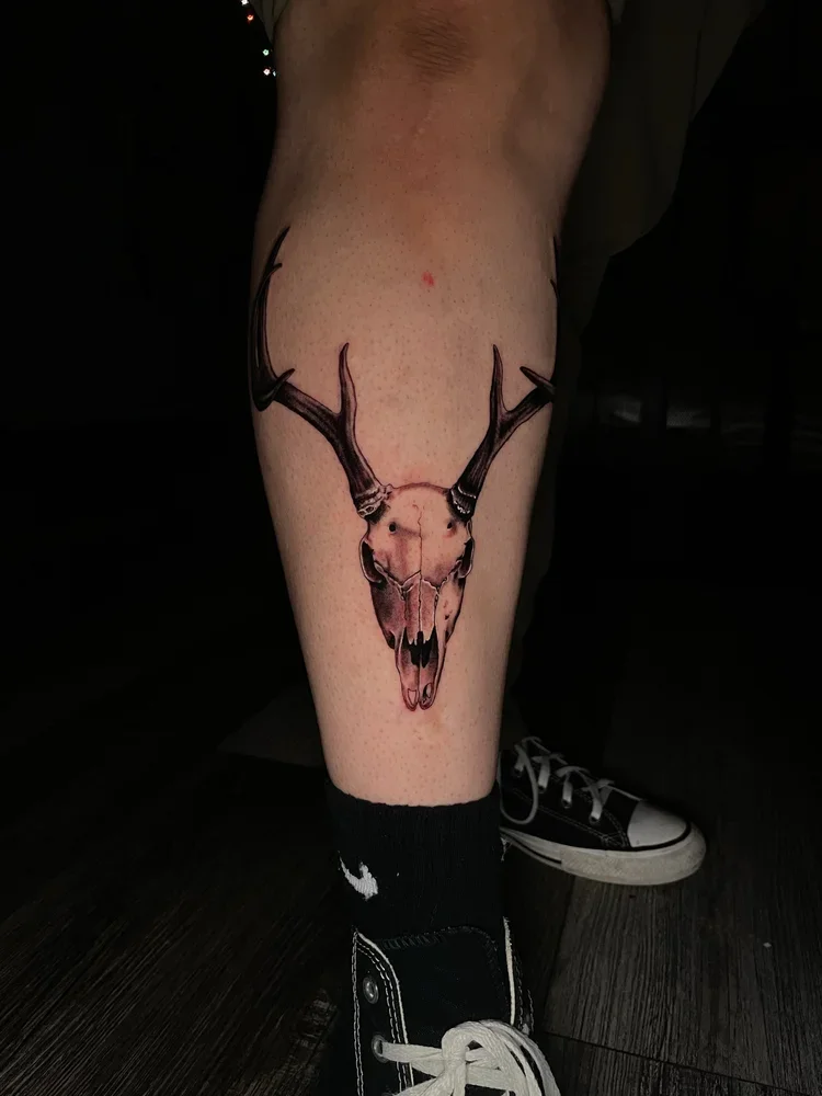 Tattoo of a deer skull with antlers on a person's calf.