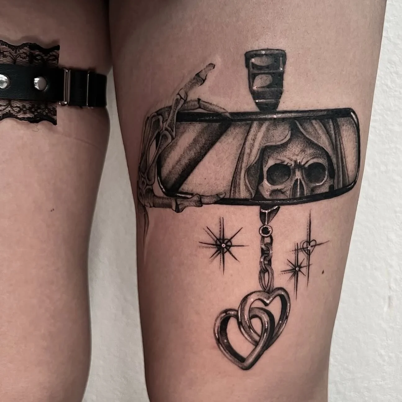Tattoo of a skeleton in a car mirror, with decorative stars, hearts, and chains.