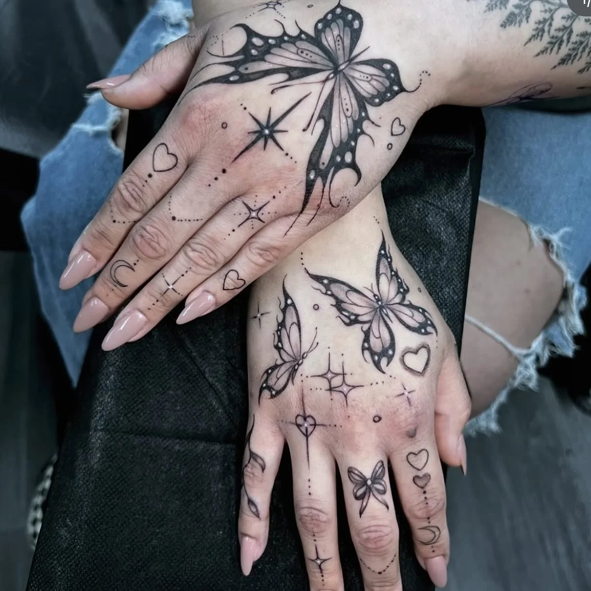 Tattooed hands with black and pink butterfly designs, hearts, stars, moon, and sparkles.