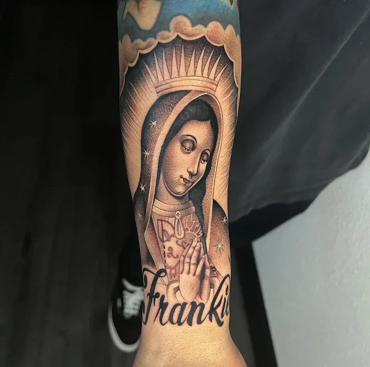 Tattoo of a religious figure, possibly the Virgin Mary, with a halo and praying hands, above the name Franklin in cursive.