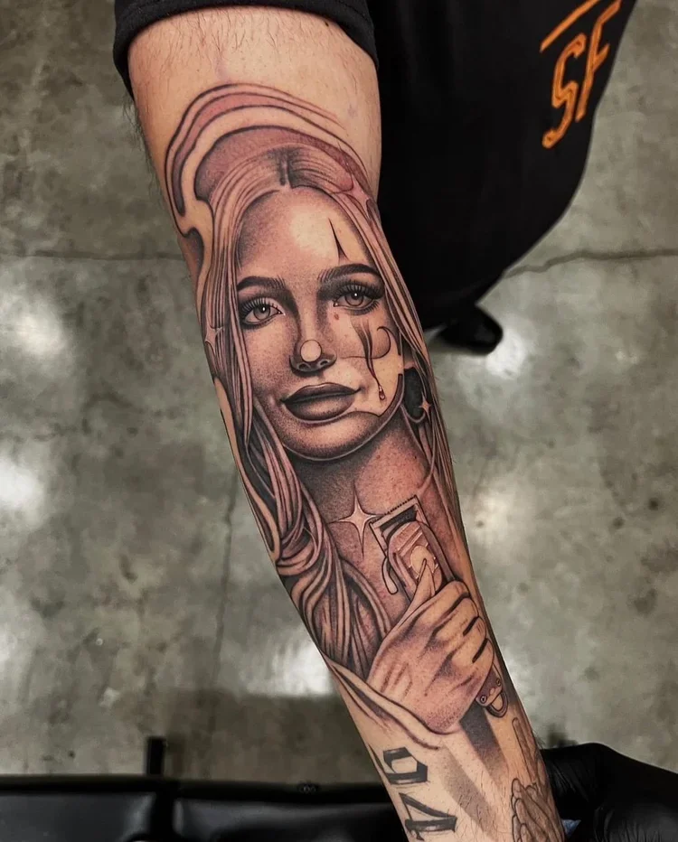 Black and gray tattoo of a woman with long hair, holding a drink with a straw, on a person's forearm.