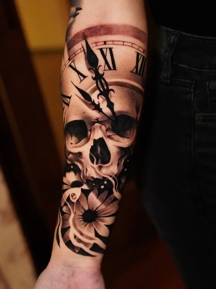 Tattoo of a skull with a clock face on the arm, featuring Roman numerals and the time showing almost 12:55, and a flower at the wrist.