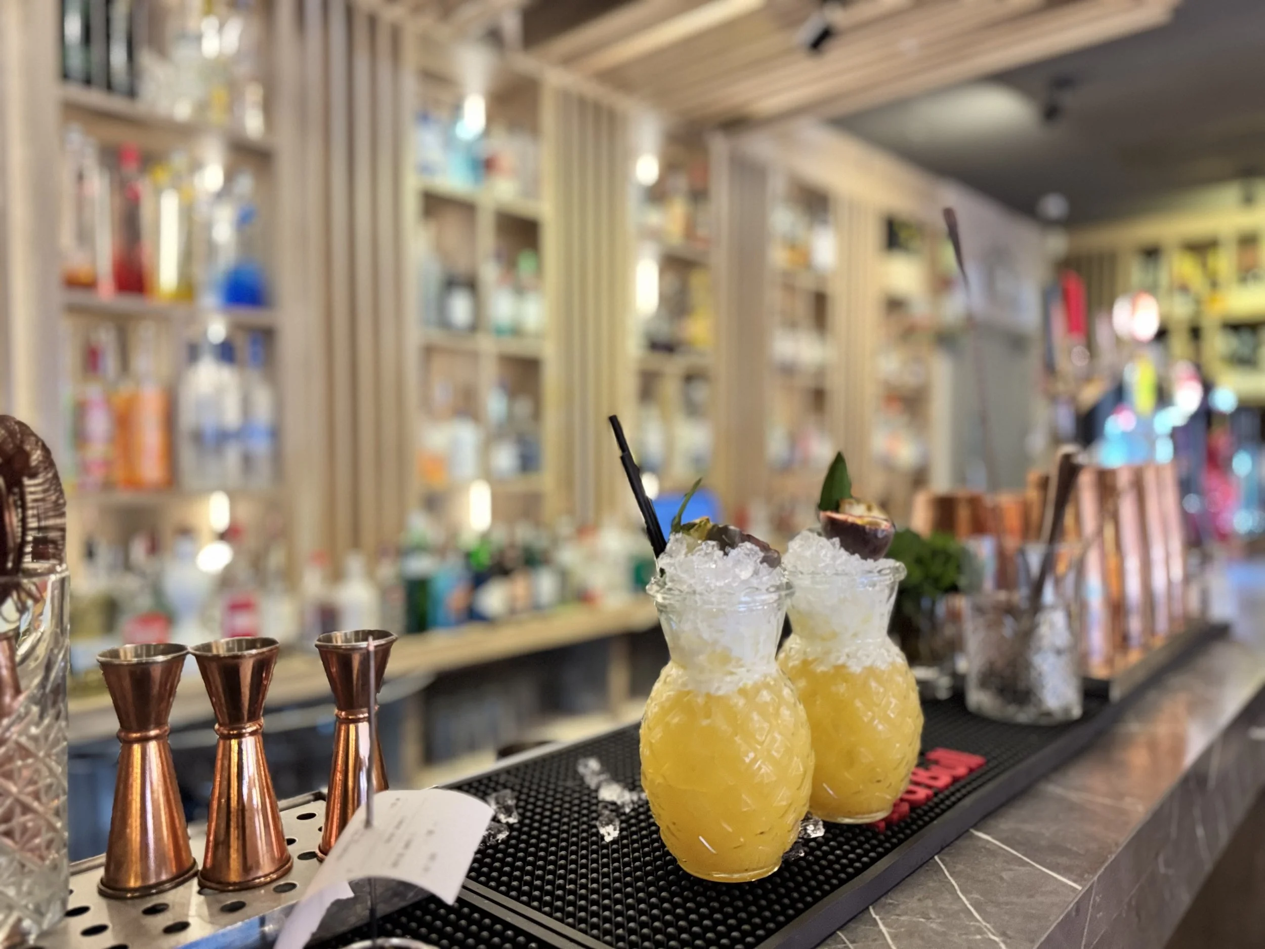 Two yellow tropical cocktails with crushed ice, garnished with lime and mint, on a bar counter.