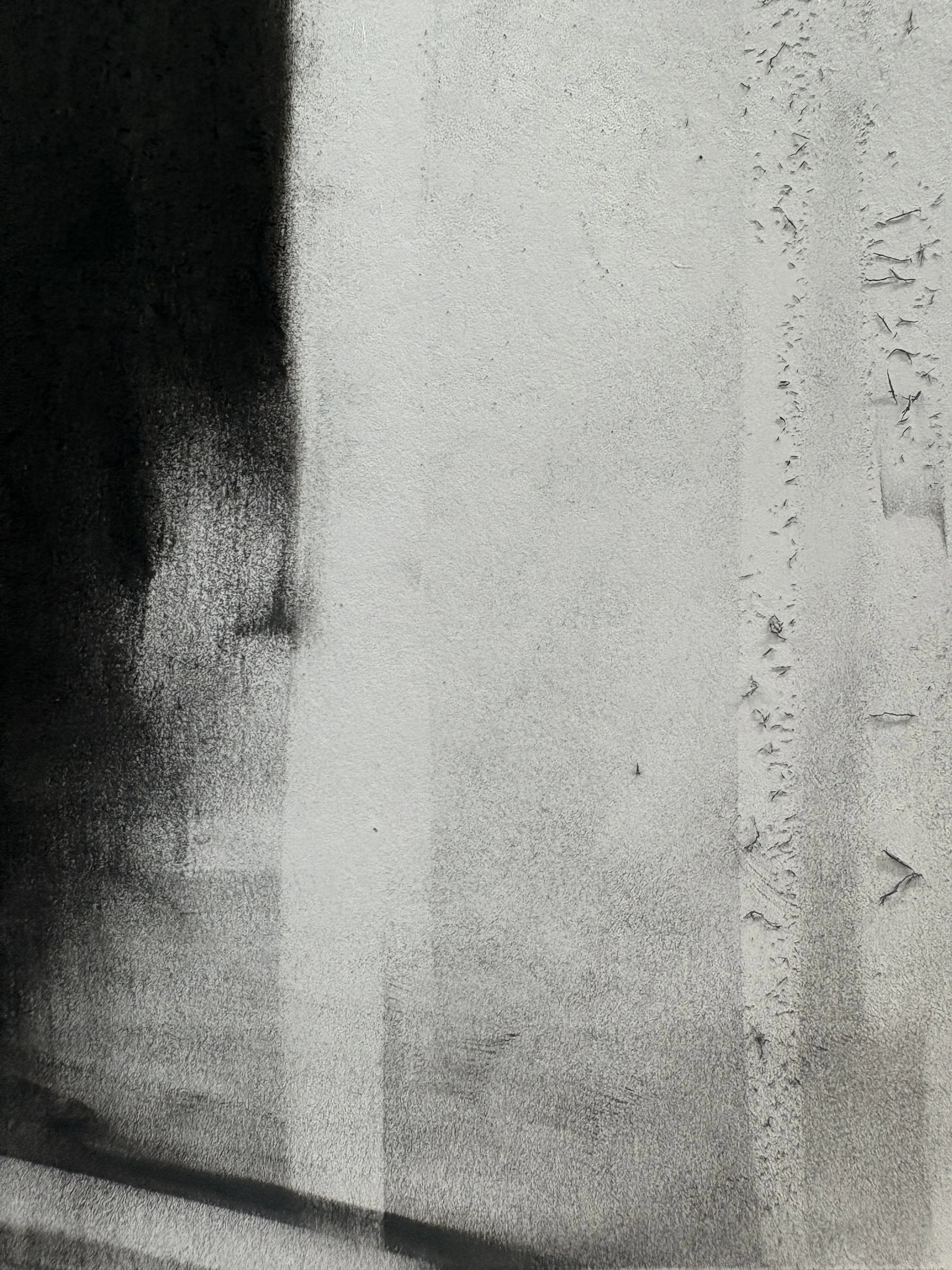 Close-up of textured paper showing a black smudge on the left side and a wavy, irregular line made of chipped charcoal on the right side.