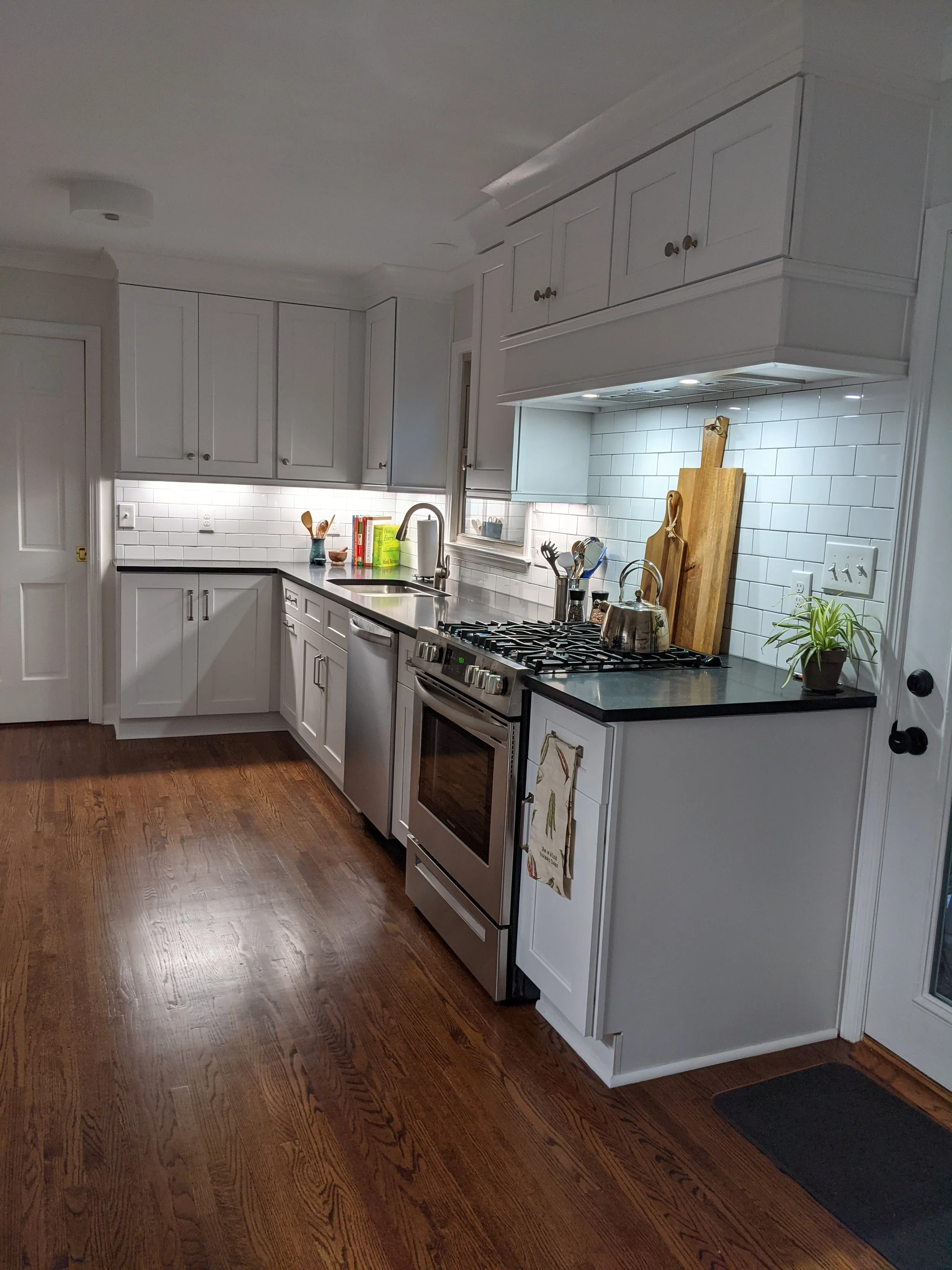 Gate Post Kitchen looking toward sink, White Shaker Cabinets, Custom Range Hood, White Subway Tile, Undercabinet Lighting.
