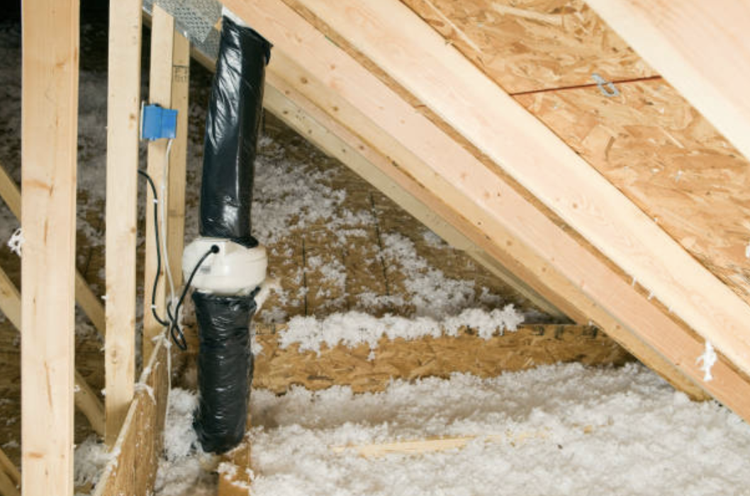 Insulation and plumbing in an unfinished attic with exposed wooden framing.