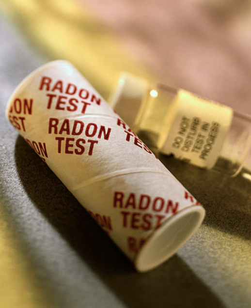 A cup with red 'RADON TEST' printed on it, lying on a dark surface with another container in the background.