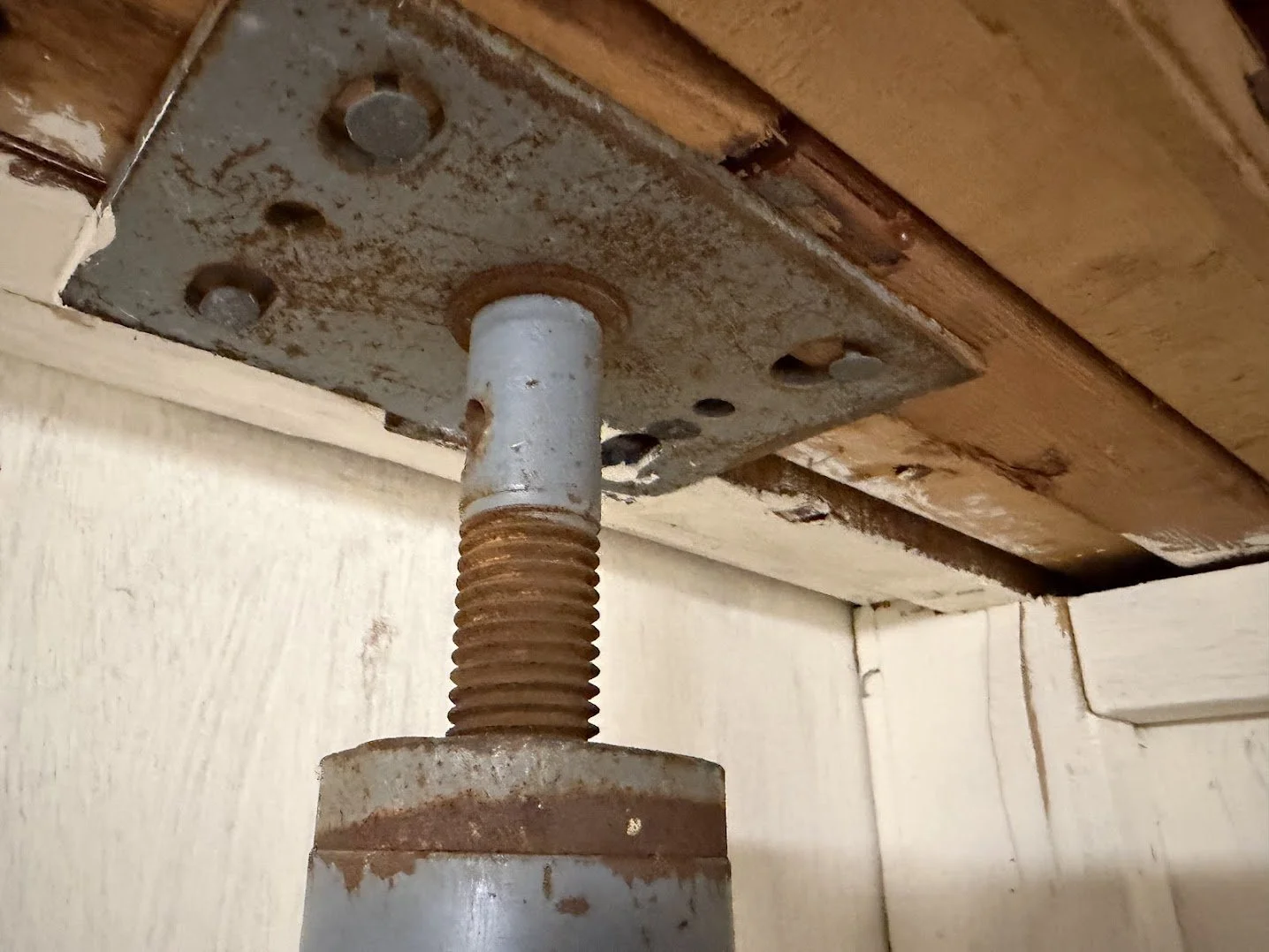 Close-up of a rusty adjustable height support screw attached to a wooden cabinet or furniture piece.