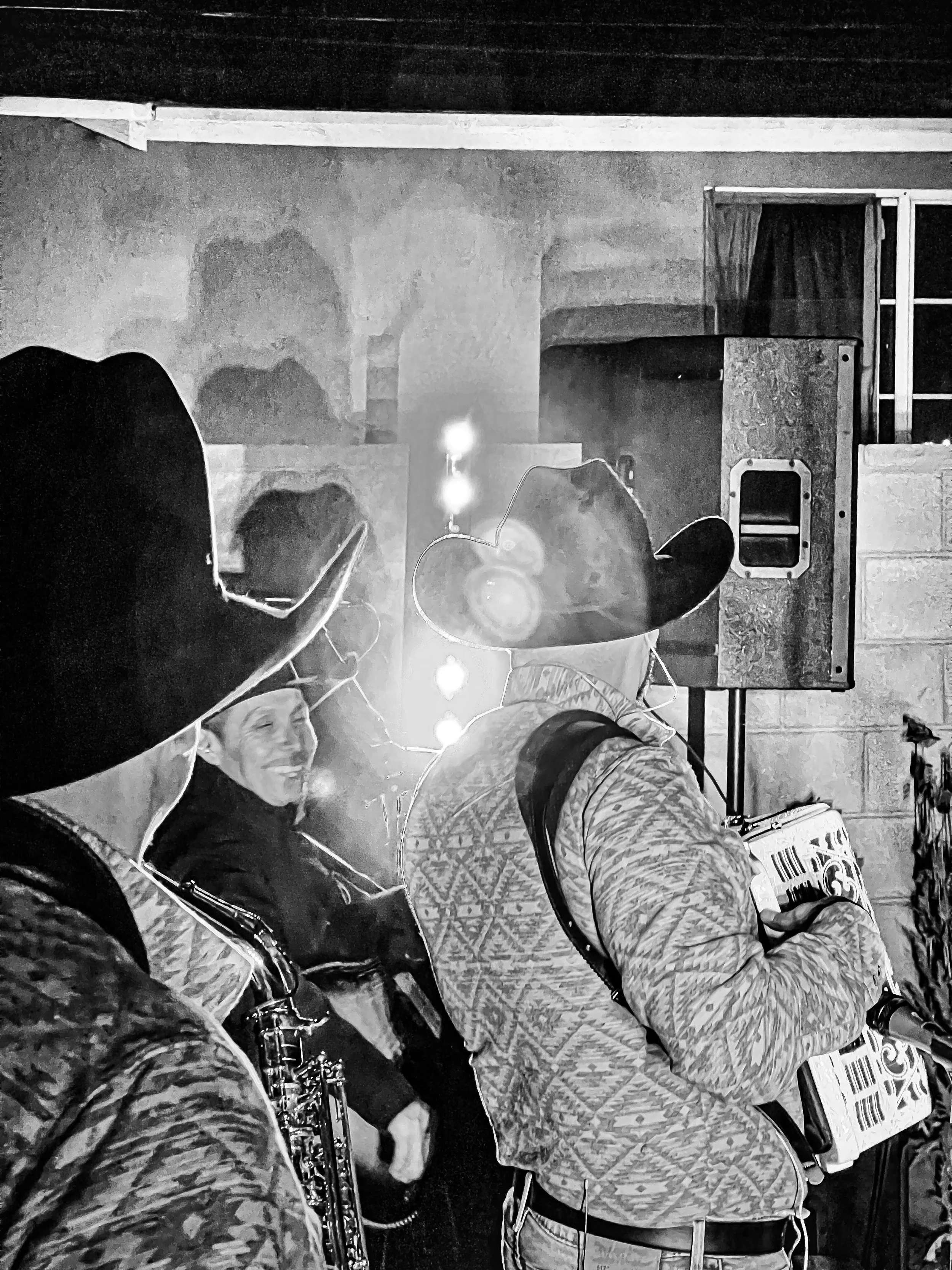 Personas en un escenario tocando instrumentos musicales en un ambiente oscuro, con un fondo de pared de ladrillos y una caja de sonido.